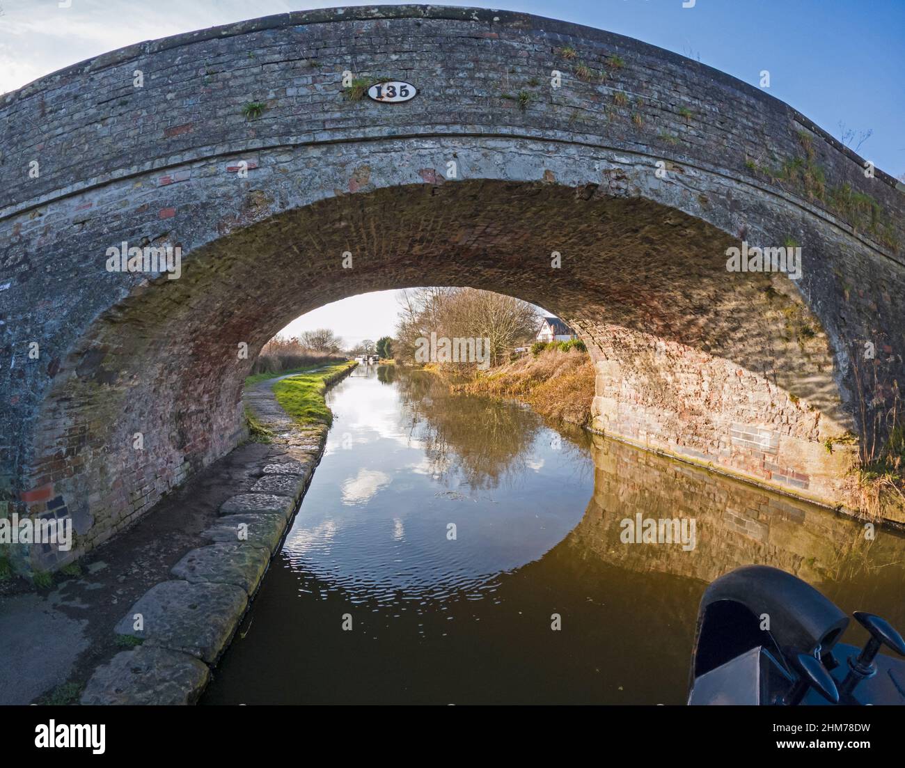 Vista dalla prua del narrowboat che mostra il paesaggio rurale inglese della campagna sul canale britannico della via d'acqua con il vecchio ponte stradale in pietra Foto Stock