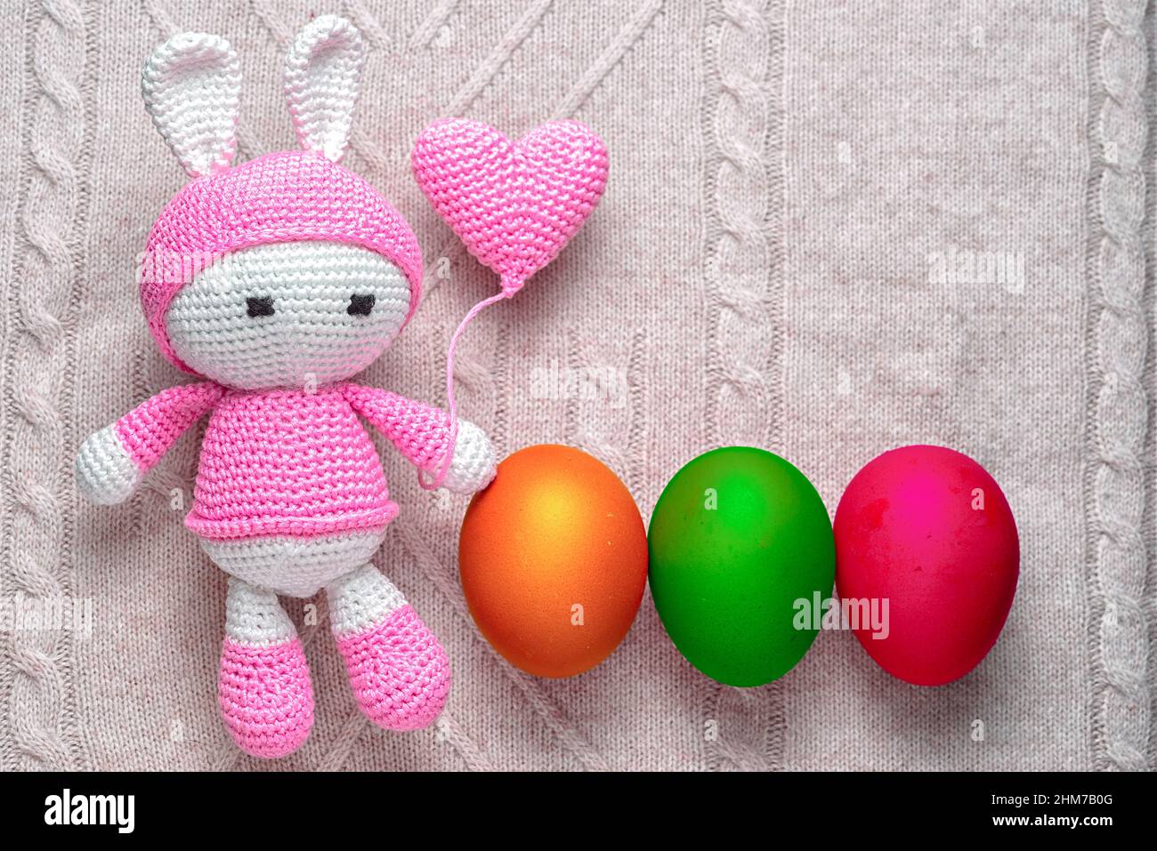 Amigurumi giocattolo coniglio di pasqua con uova colorate in fila su uno sfondo lavorato a maglia - carta di pasqua con spazio copia Foto Stock