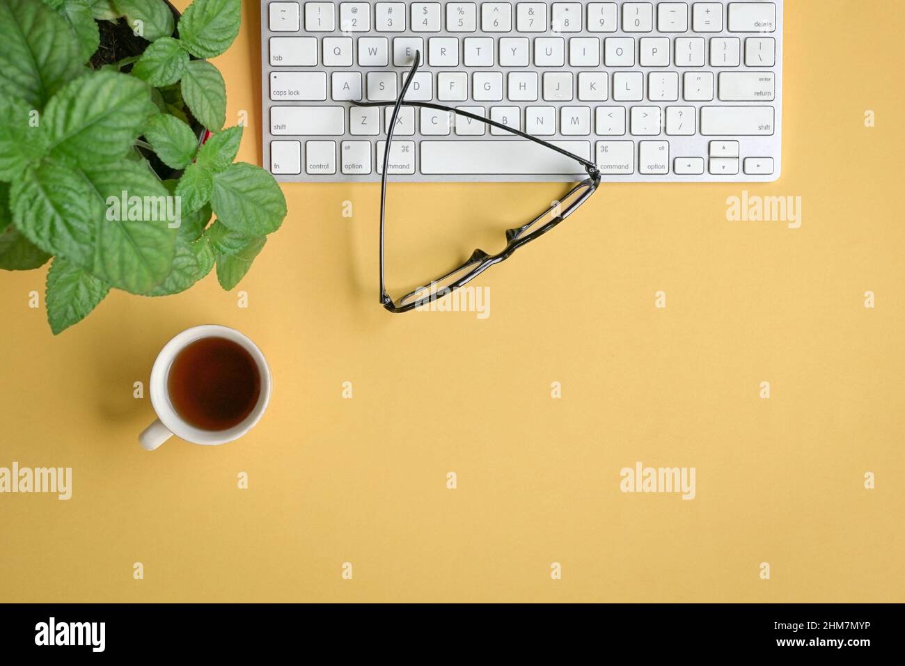 Vista dall'alto della scrivania gialla con tastiera, occhiali, caffè e piante. Spazio di copia. Foto Stock