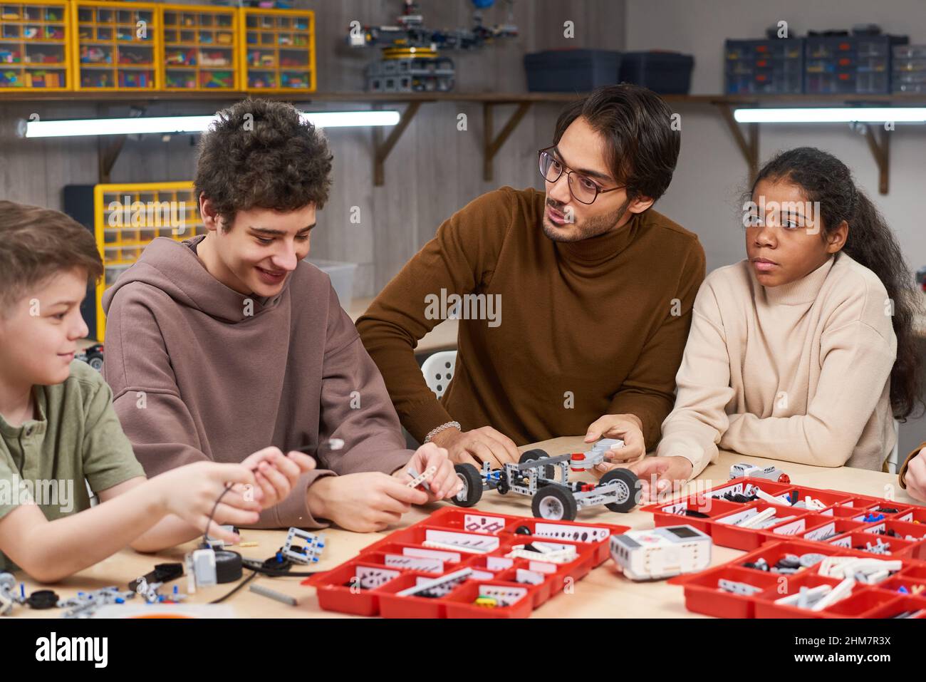 Ritratto di giovane insegnante di sesso maschile che aiuta diversi gruppi di bambini che costruisce robot in classe di ingegneria a scuola Foto Stock
