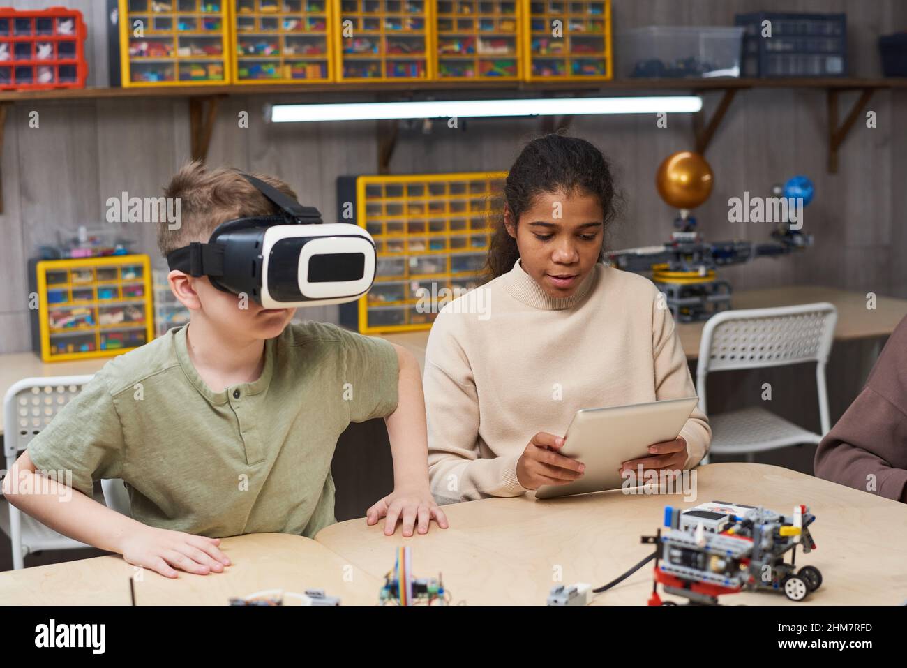 Team di due bambini che costruiscono robot insieme e utilizzano attrezzature per la realtà virtuale mentre si diverse a scuola con la lezione di ingegneria Foto Stock