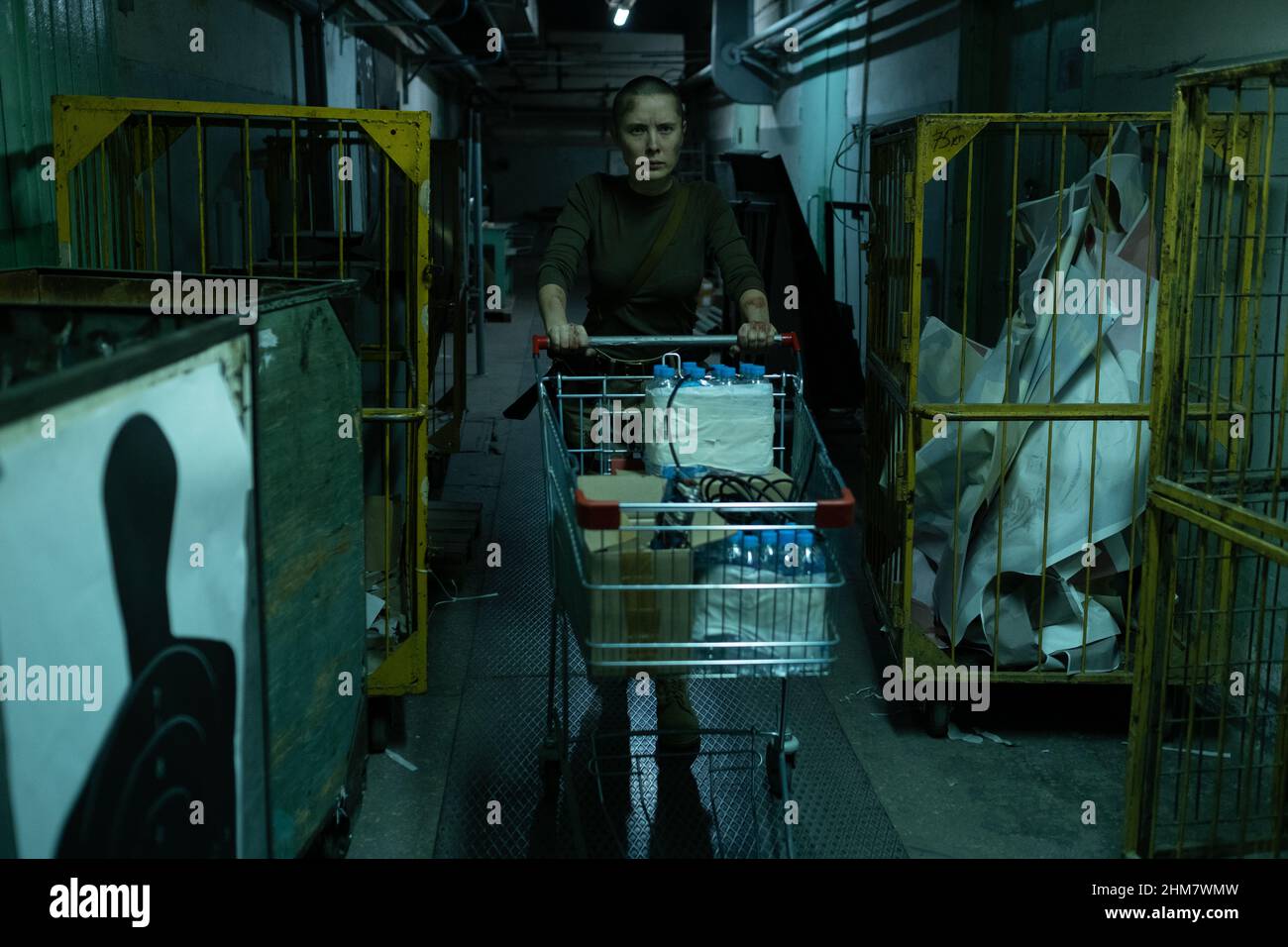 Ritratto di donna resistente carrello di spinta con kit di sopravvivenza e acqua in corridoio industriale scuro, spazio copia Foto Stock