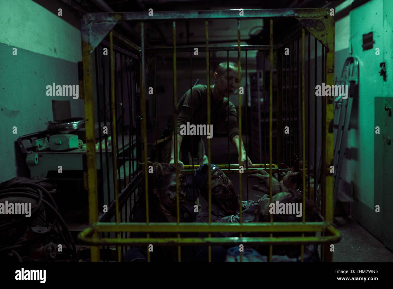Ritratto di donna dura tirando gabbia con zombie in buio ambiente industriale, post apocalittico sopravvivenza concetto, copia spazio Foto Stock