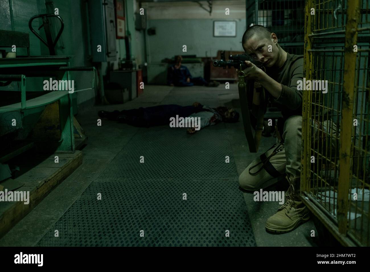 Ritratto a tutta lunghezza di una dura soldato femminile puntando la pistola alla macchina fotografica in corridoio industriale scuro con zombie in background, spazio copia Foto Stock