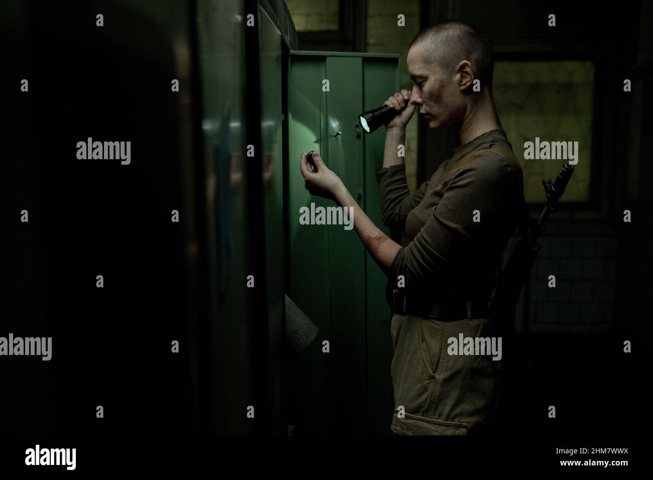 Vista laterale ritratto di resistente donna sopravvissuto ricerca armadietti con torcia in camera industriale scuro, spazio copia Foto Stock