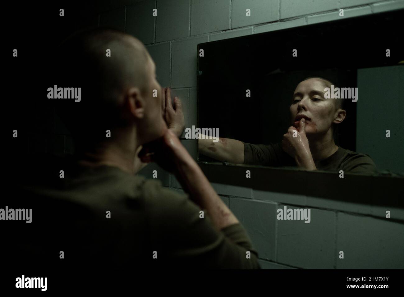 Ritratto di giovane donna dura guardando lo specchio e spazzando il sangue via la faccia in buio di sopravvivenza impostazione, copia spazio Foto Stock