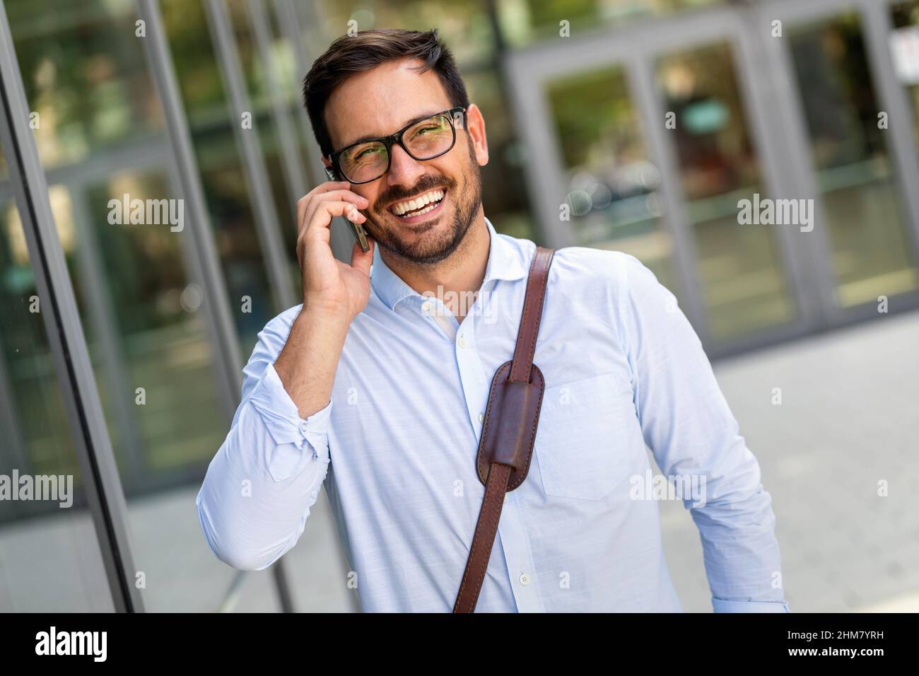 Bell'uomo d'affari di successo che usa lo smartphone davanti all'ufficio. Concetto di business tecnologico. Foto Stock