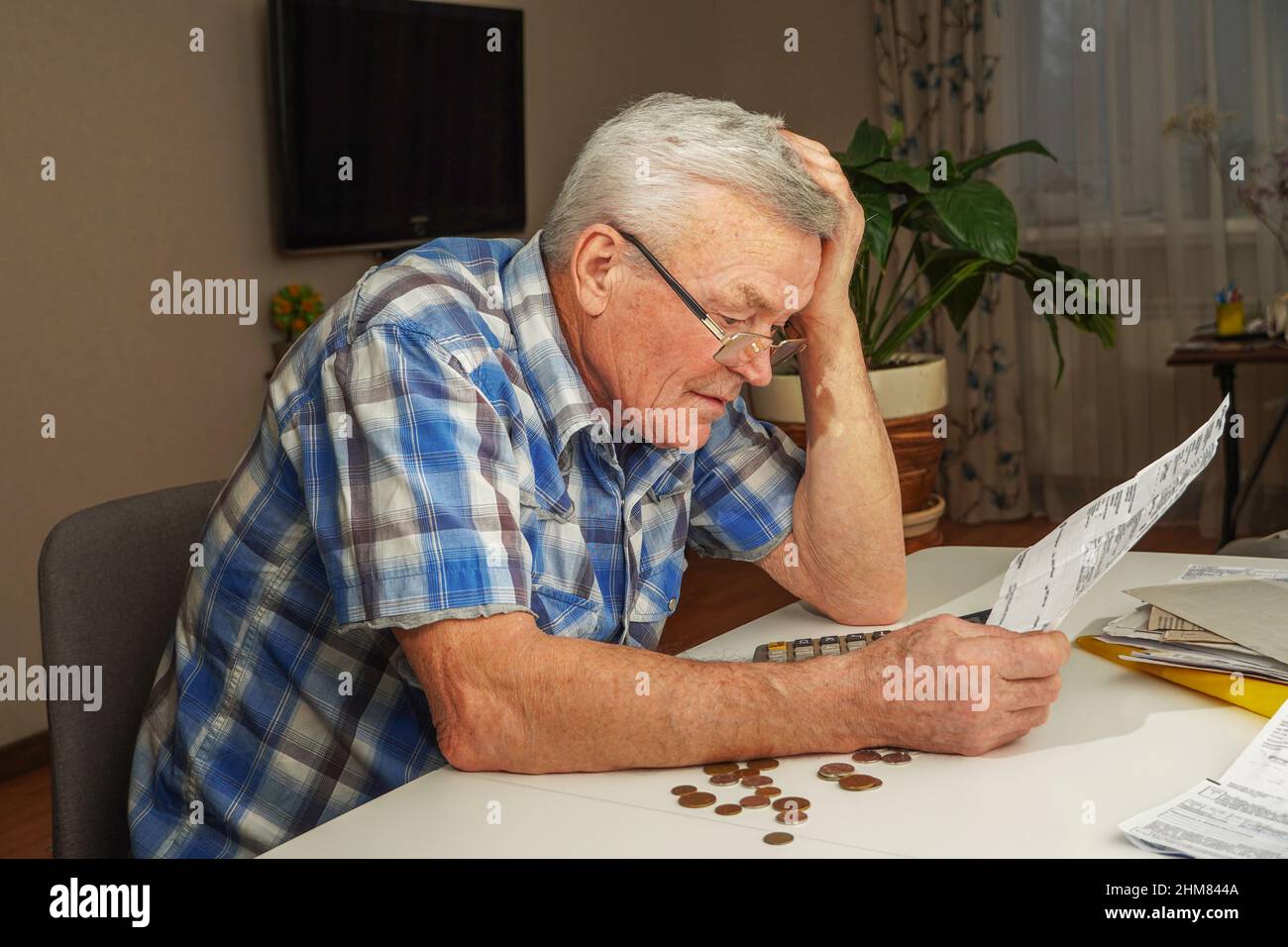 Sconvolto uomo anziano depresso seduto al tavolo e calcolando le finanze. Vecchio controllo fatture. Uomo che conta le monete sul tavolo. Calcolo della pensione Foto Stock
