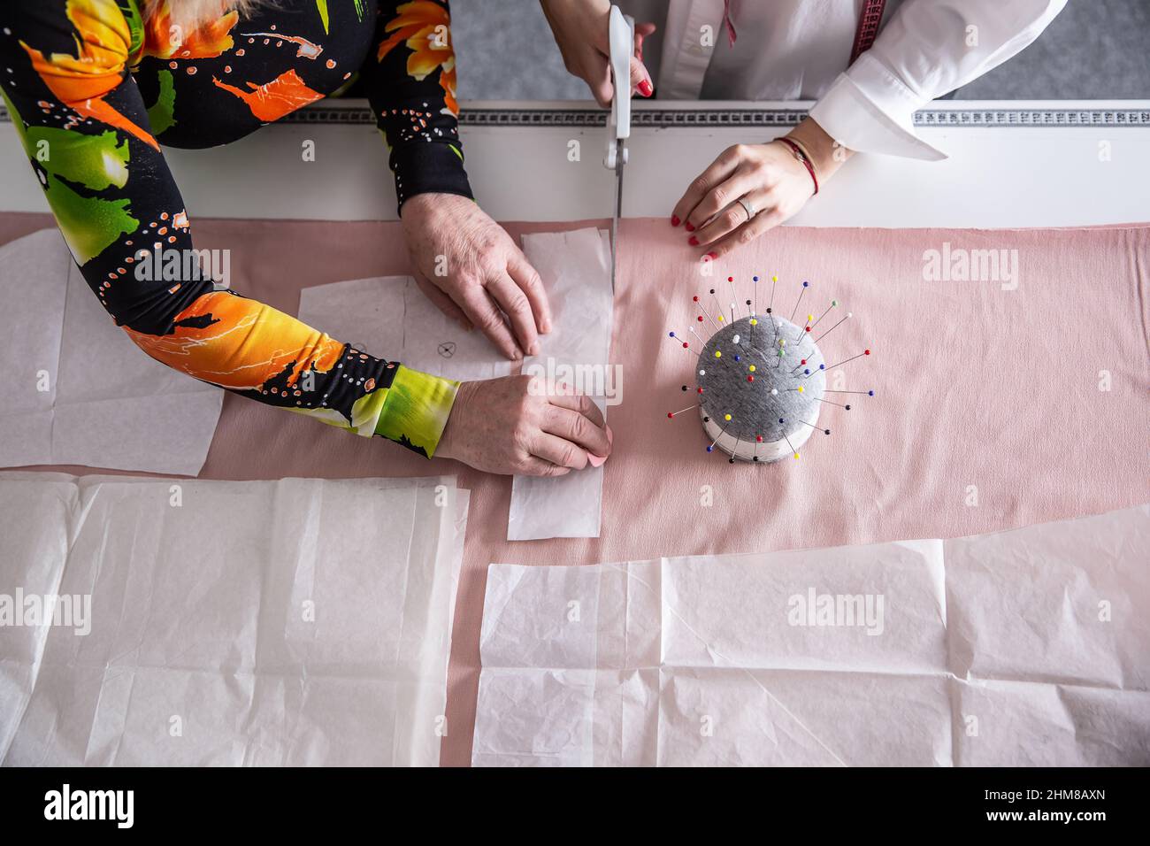 Vista dall'alto del lavoro di sarti in officina misurazione, taglio e cucitura di abiti dal tessuto sul tavolo in base a modello di carta. Foto Stock