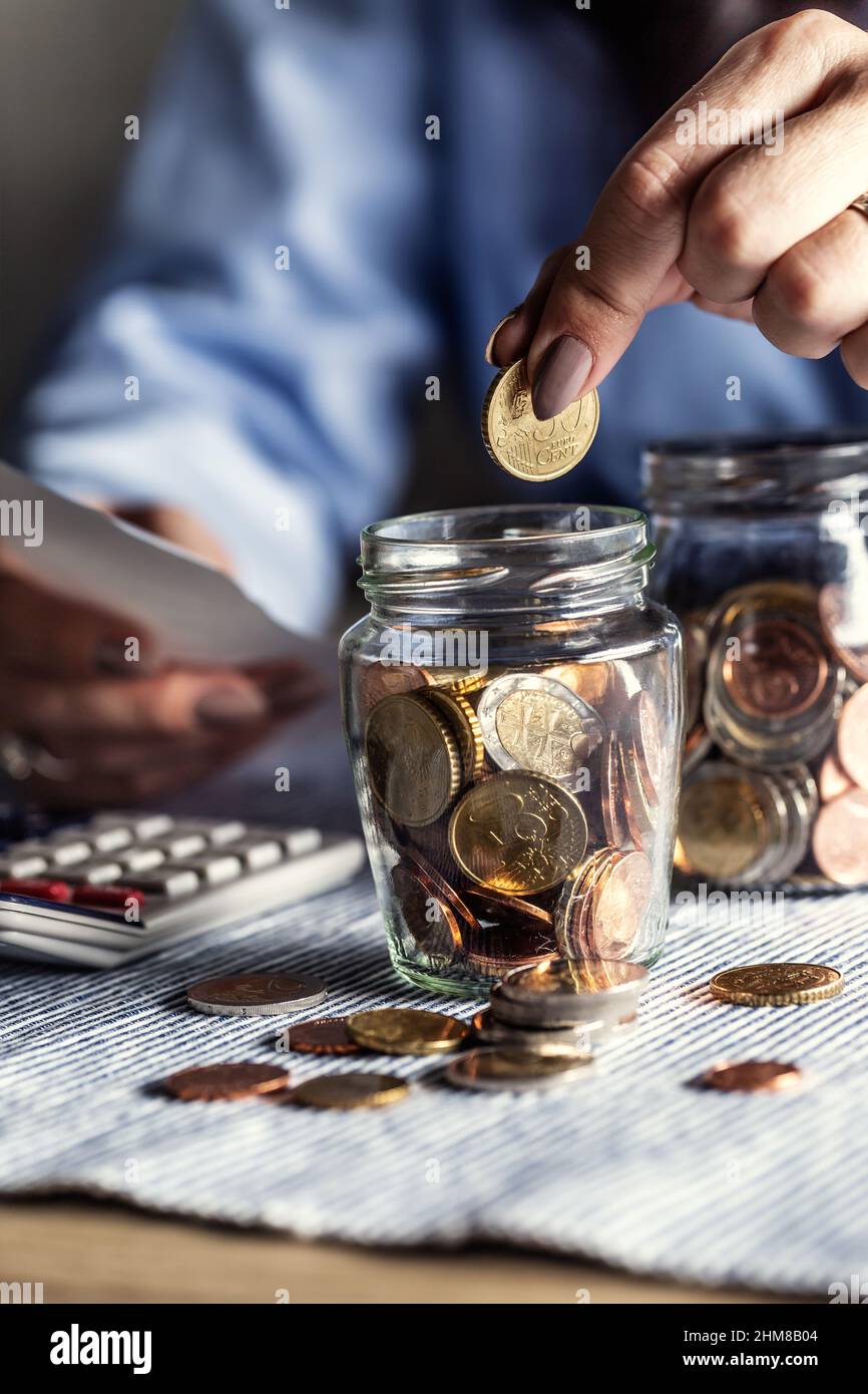 Mettendo 50 centesimi in un barattolo di monete in euro da una donna che conta le fatture. Foto Stock