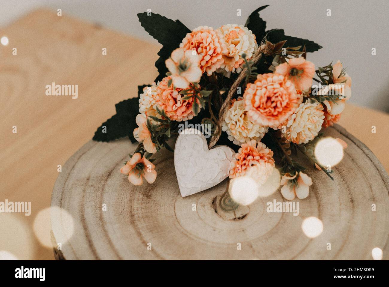 tavolo di legno con un bouquet di fiori e un cuore bianco e bokeh luci intorno ad esso. Foto Stock