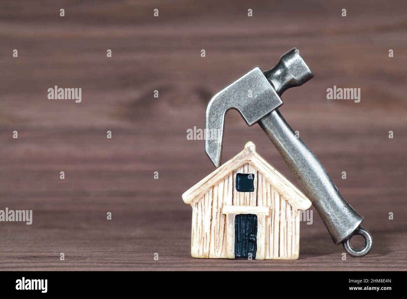 Martello in acciaio adagiato su una casa giocattolo in miniatura su sfondo di legno. Pianificazione di una grande ristrutturazione casa. Foto Stock