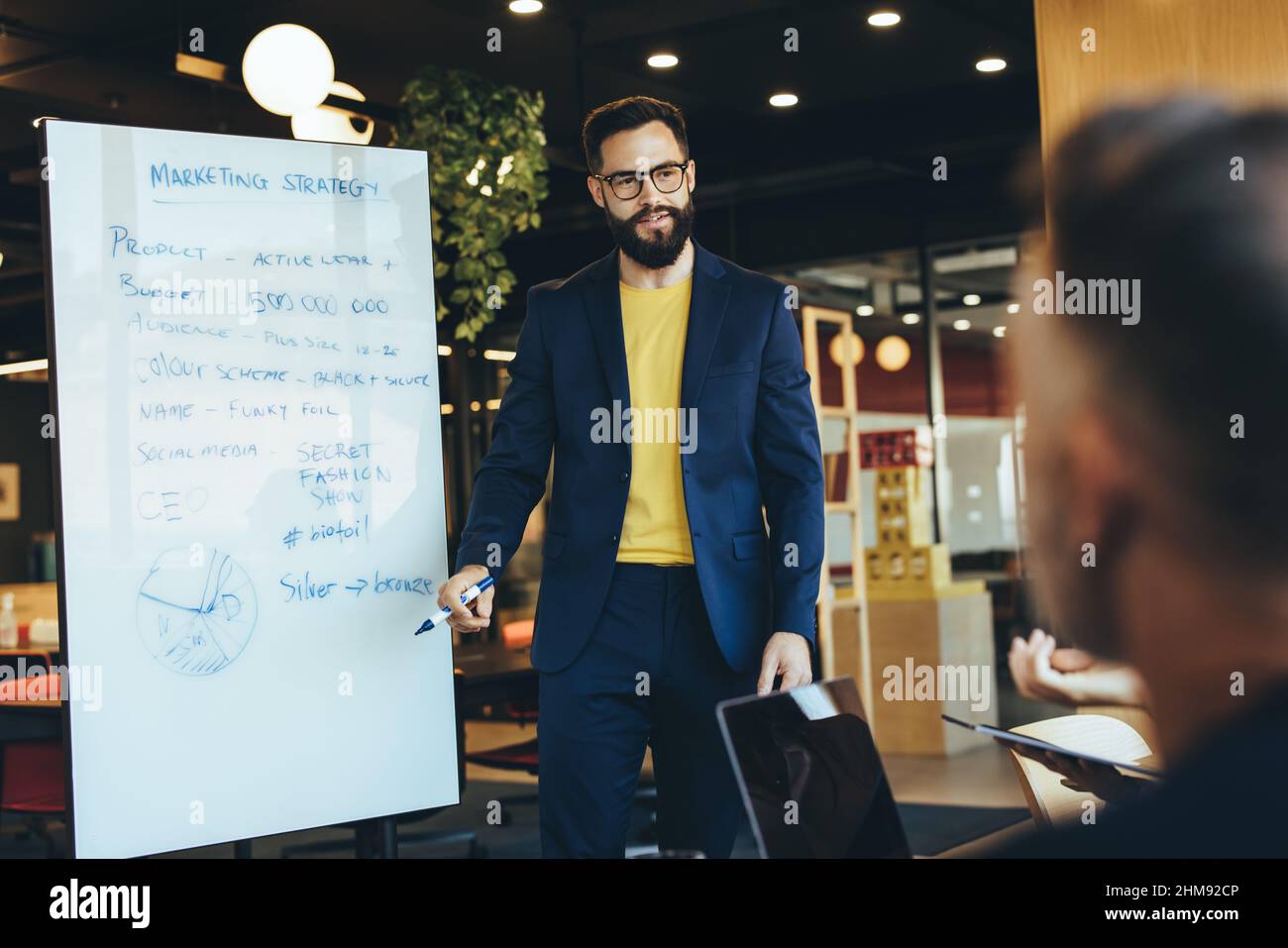 responsabile aziendale che tiene una presentazione durante una riunione con il suo team. Giovane uomo d'affari fiducioso che discute la sua strategia di marketing con il suo colleagu Foto Stock