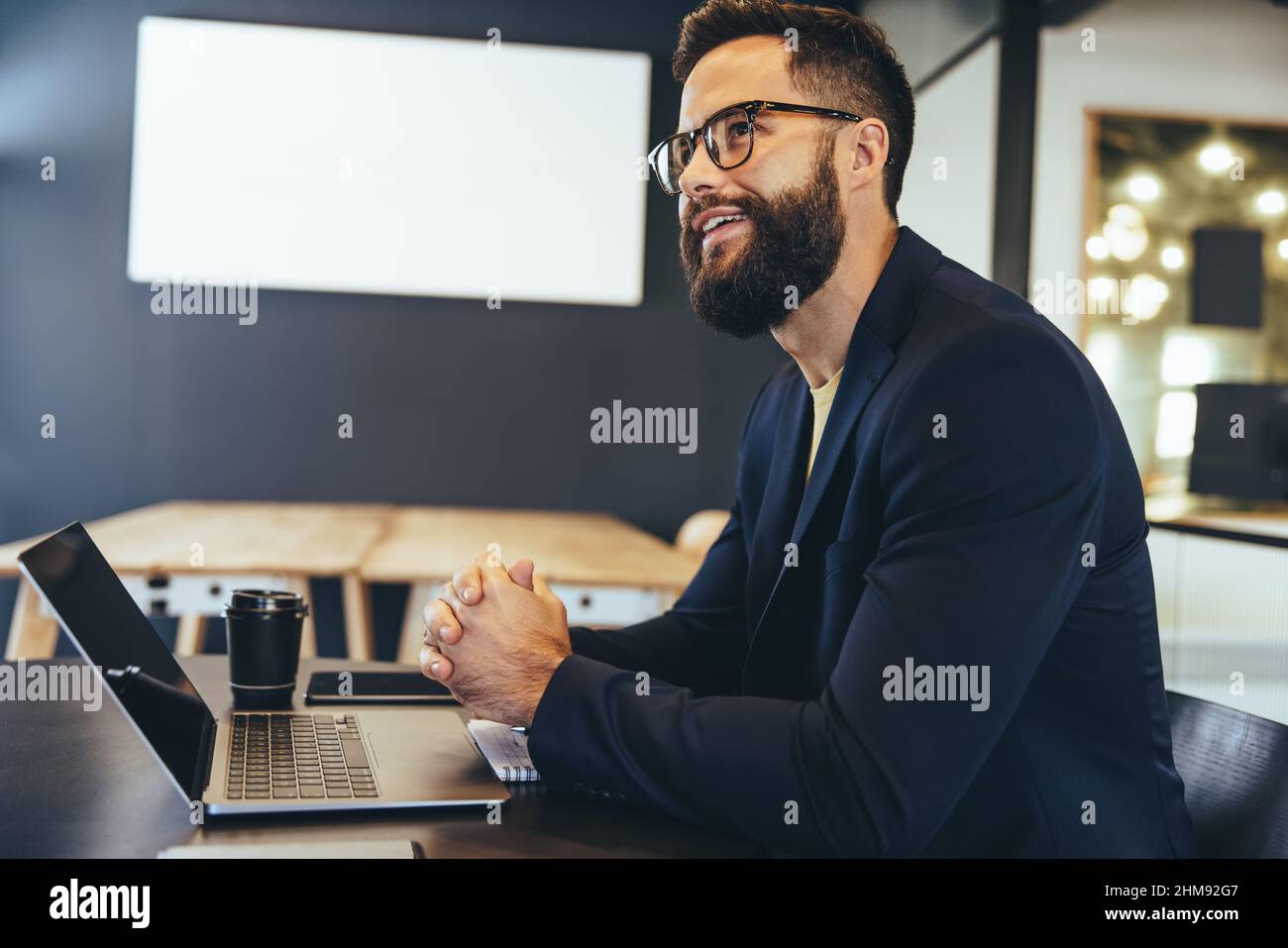 Uomo d'affari attento seduto da solo in un ufficio. Felice giovane imprenditore sorridente mentre contempla nuove idee di affari. Lavoro di imprenditore allegro Foto Stock