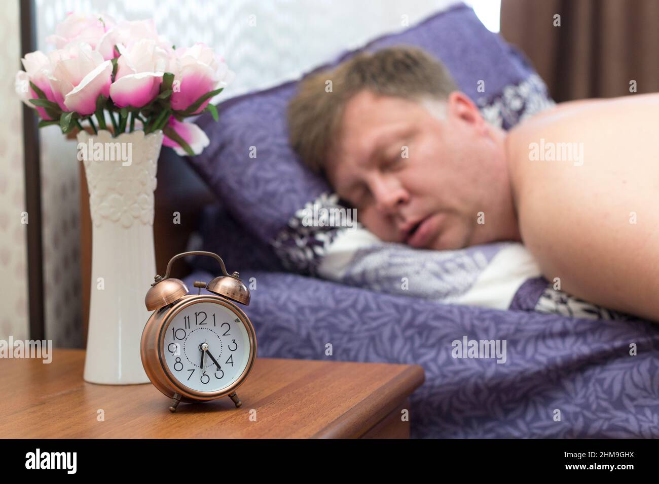 Un uomo adulto di 40-45 anni si addormentò rapidamente nel suo letto senza sentire la sveglia. Foto Stock