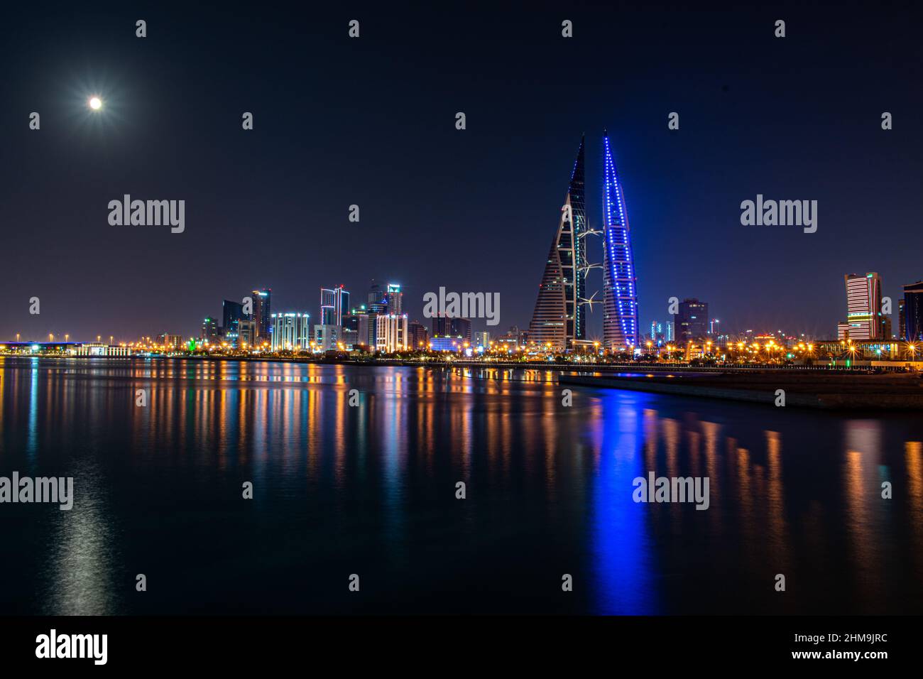 Una luna piena brilla sullo skyline di Manama, Bahrain, mentre le luci per il World Trade Center e gli edifici circostanti riflettono al largo del mare. Foto Stock