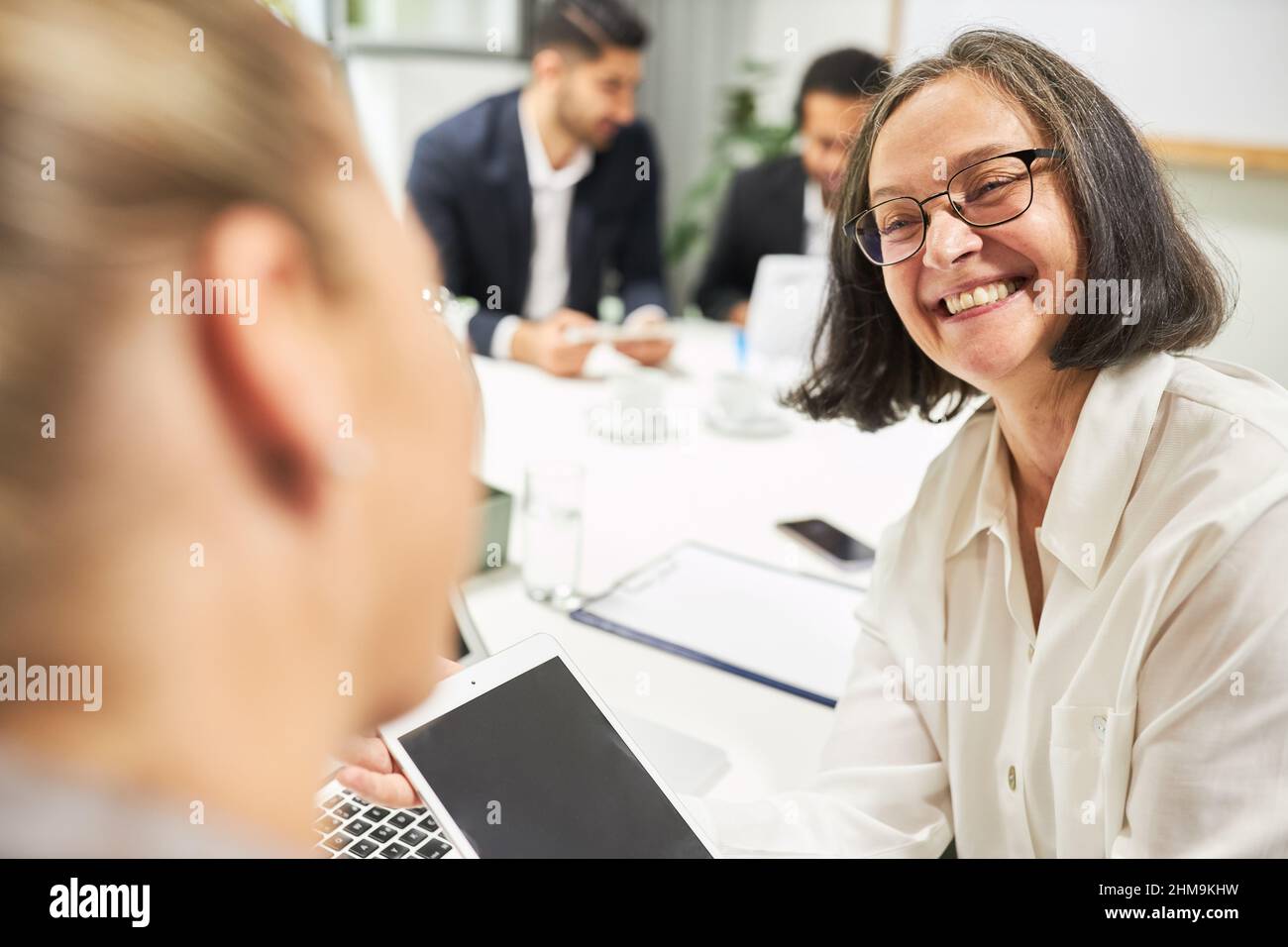 Anziana donna d'affari come insegnante con un computer tablet in un laboratorio di computer insieme ad un tirocinante Foto Stock