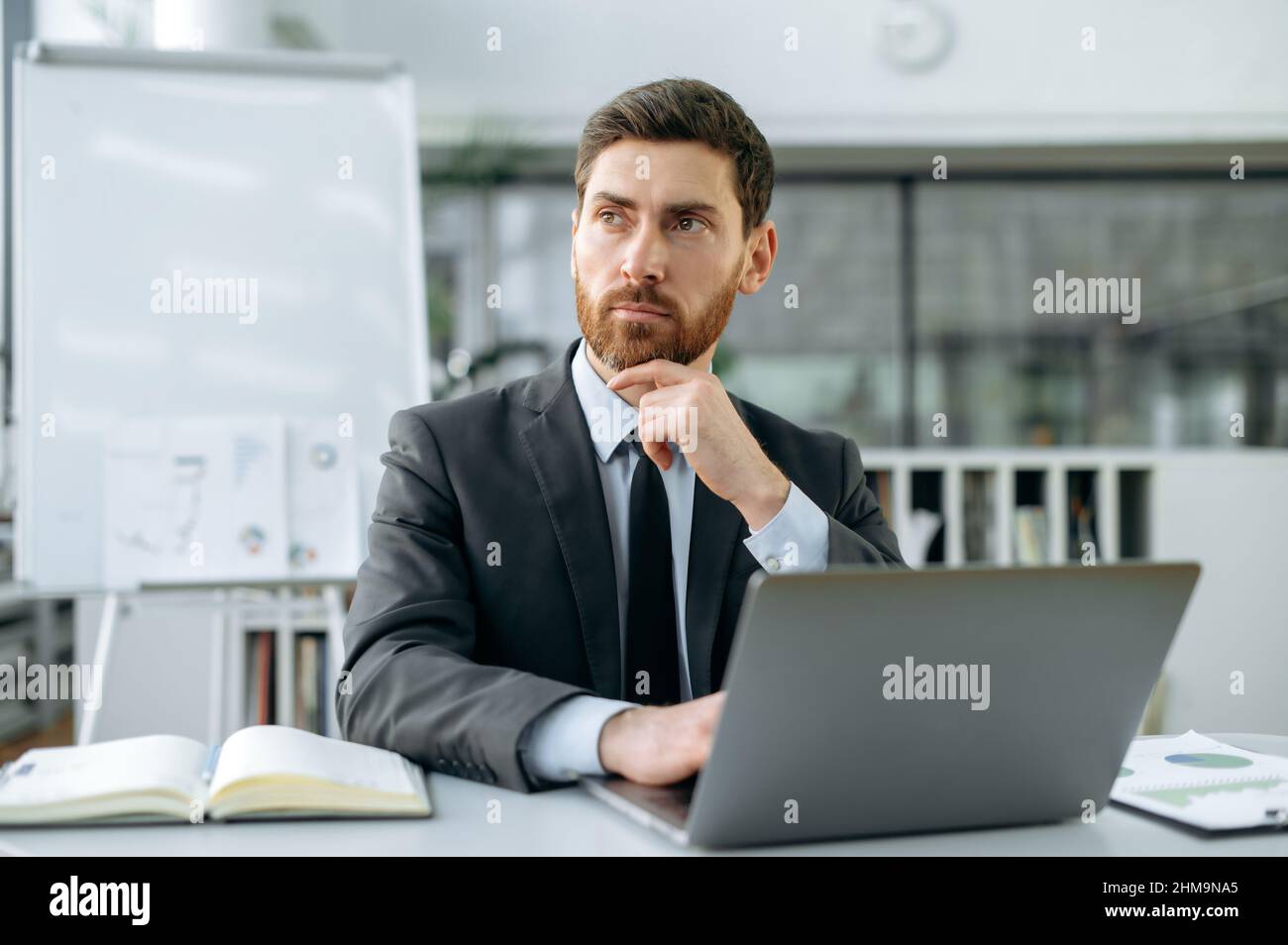 L'imprenditore maschile caucasico intelligente pensivo, direttore finanziario, ceo, in tuta formale, si siede alla scrivania in un ufficio moderno, guarda via, pensando a un nuovo progetto, strategia aziendale, idee di marketing Foto Stock