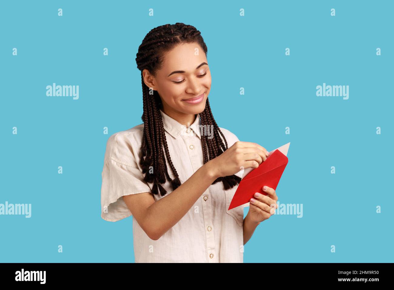 Ritratto di donna sorridente con predellini neri in piedi busta rossa aperta con congratulazioni, lettura lettera romantica, indossare camicia bianca. Studio interno girato isolato su sfondo blu. Foto Stock