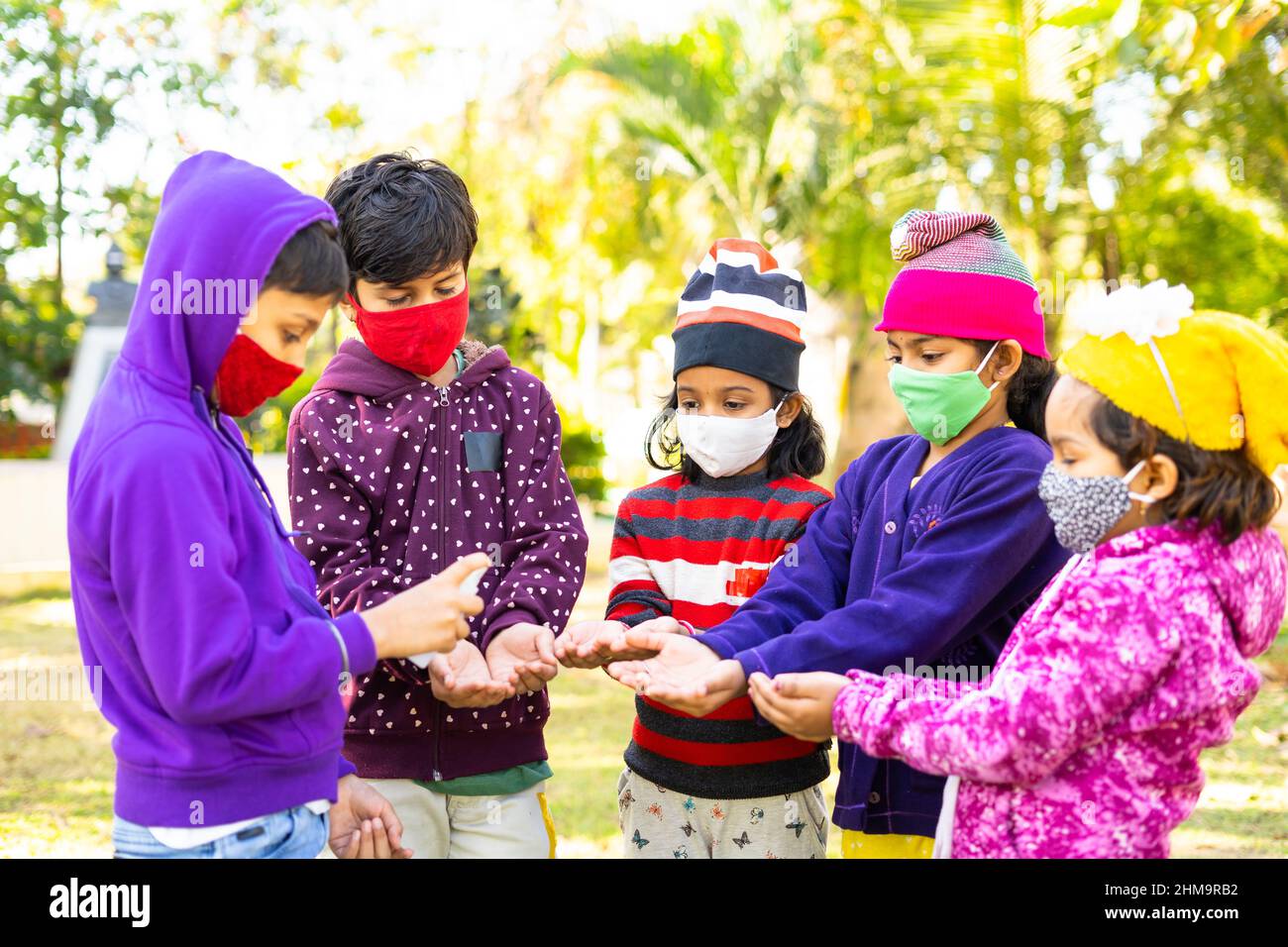 Focus sul bambino anteriore, Bambini con maschera medica viso lavando le mani con disinfettante disinfettante a causa di coronavirus pandemic al parco - concetto di convivid-19 Foto Stock