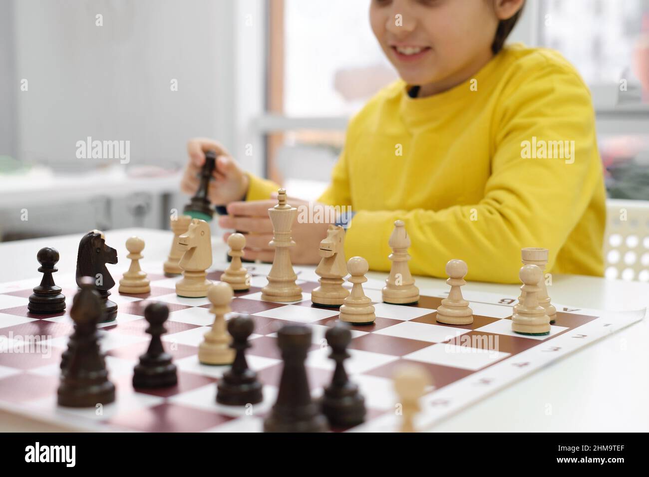 Mano closeup ragazzo caucasico giocare a scacchi. Bambino concentrato felice dietro gli scacchi in lezione di classe o di scuola. Eccitato ragazzo della scuola elementare intelligente con Foto Stock