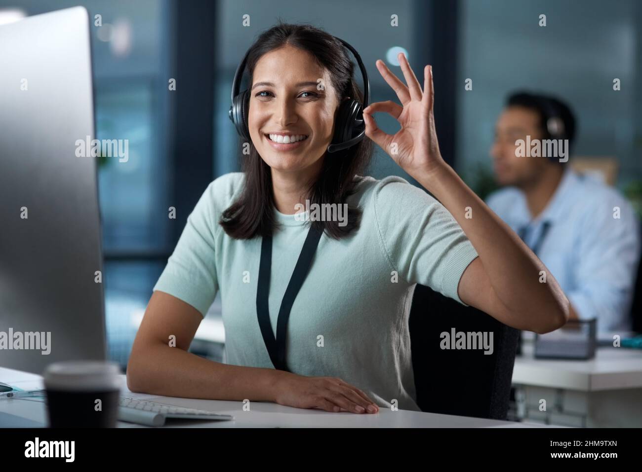 Non c'è da stupirsi che siano stati valutati i migliori nel servizio clienti. Ritratto di una giovane donna con una cuffia e mostrando un gesto OK in un ufficio moderno. Foto Stock