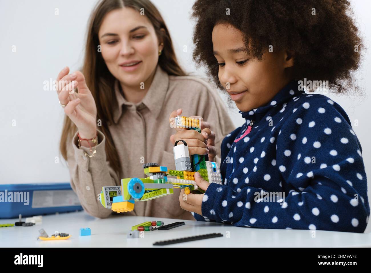 Classe di codifica, scuola ragazza costruire robot braccio meccanismo. Bambini multietnici fare scienza, la tecnologia compiti con tablet. Istruzione moderna Foto Stock