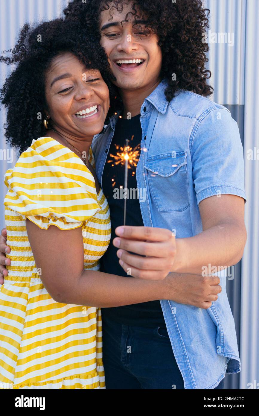 Gioiosa coppia ispanica con ricci afro abbracciando teneramente e scintillio ardente per un'occasione speciale di festa Foto Stock