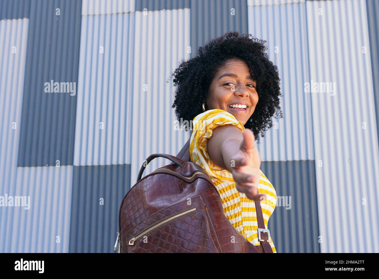 Vista posteriore della femmina ispanica con capelli ricci sorridendo piacevolmente mentre si raggiunge la mano per il supporto e guardando la macchina fotografica Foto Stock