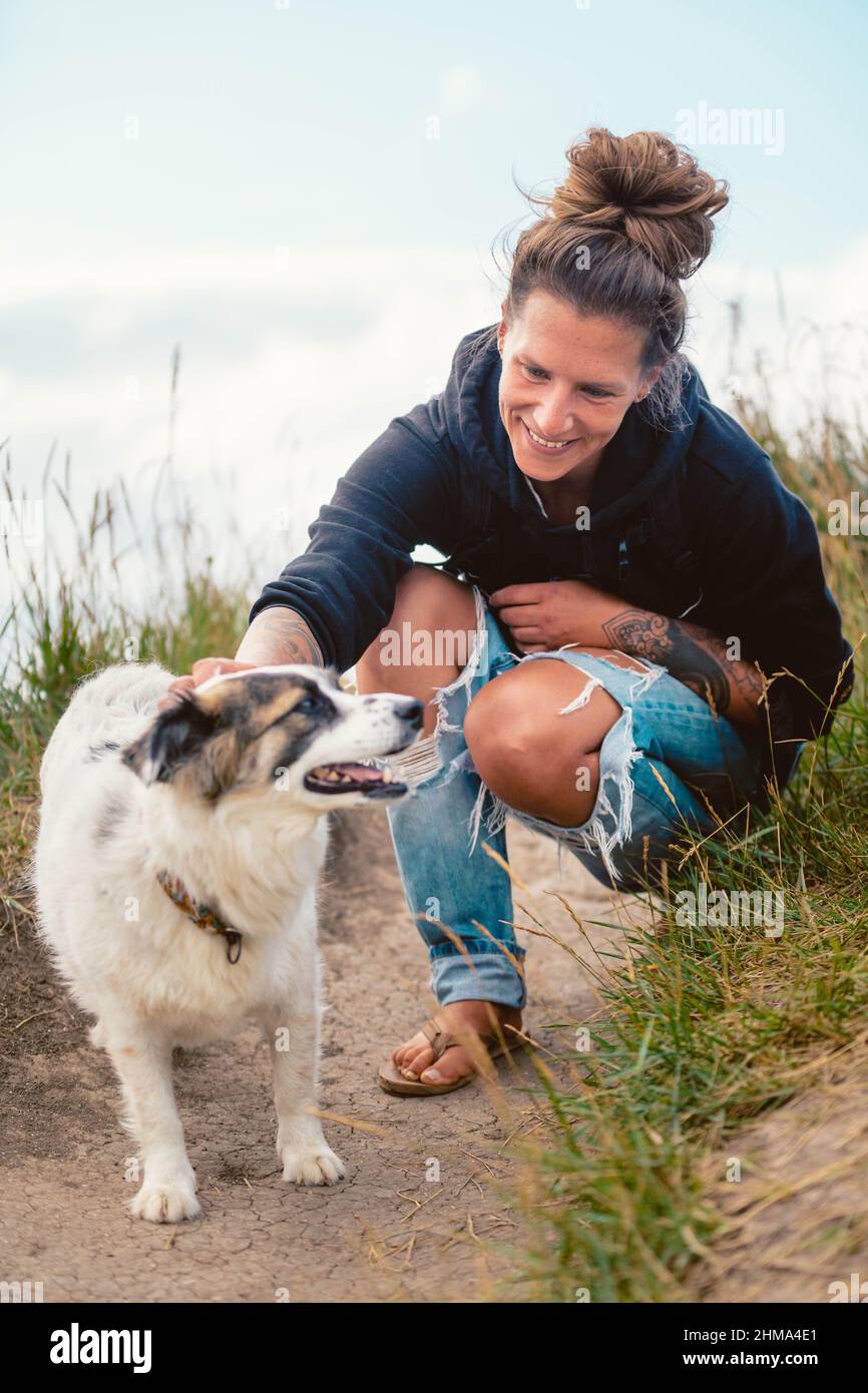 Positiva donna proprietario seduto su fienili e accarezzare confine obbediente Collie sul sentiero durante la passeggiata in prato erboso in Cantabria Foto Stock