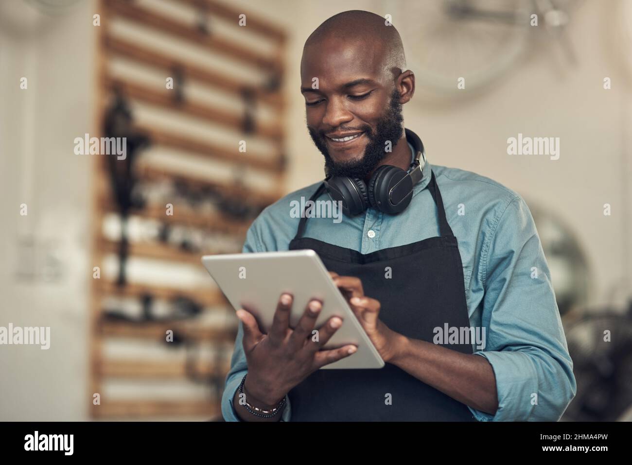 I client stanno già inviando un'e-mail. Girato di un bel giovane uomo in piedi da solo nel suo negozio di biciclette e utilizzando un tablet digitale. Foto Stock