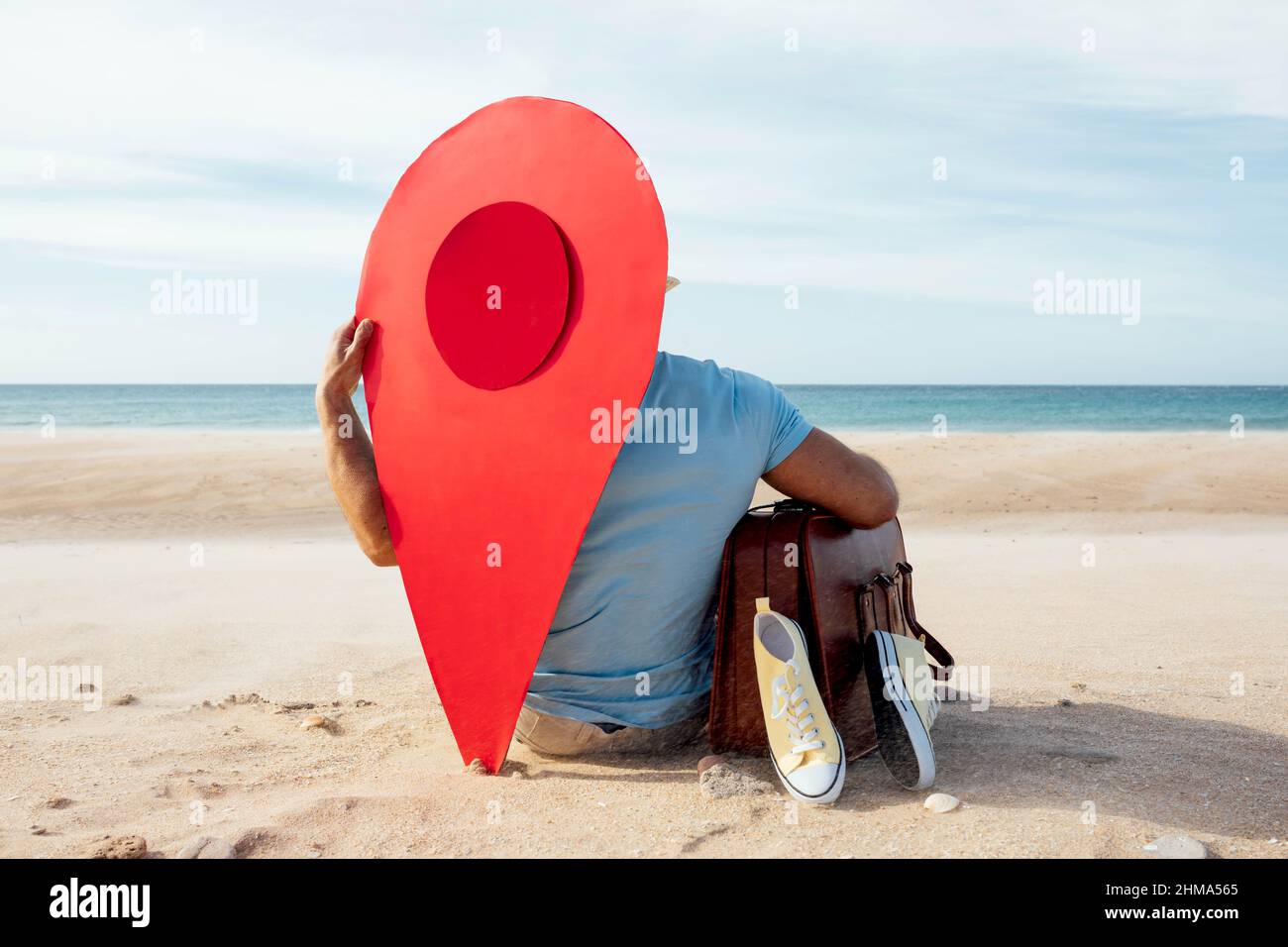 Vista posteriore dell'irriconoscibile turista maschile seduto con bagaglio e puntatore rosso mappa sulla spiaggia sabbiosa in estate Foto Stock