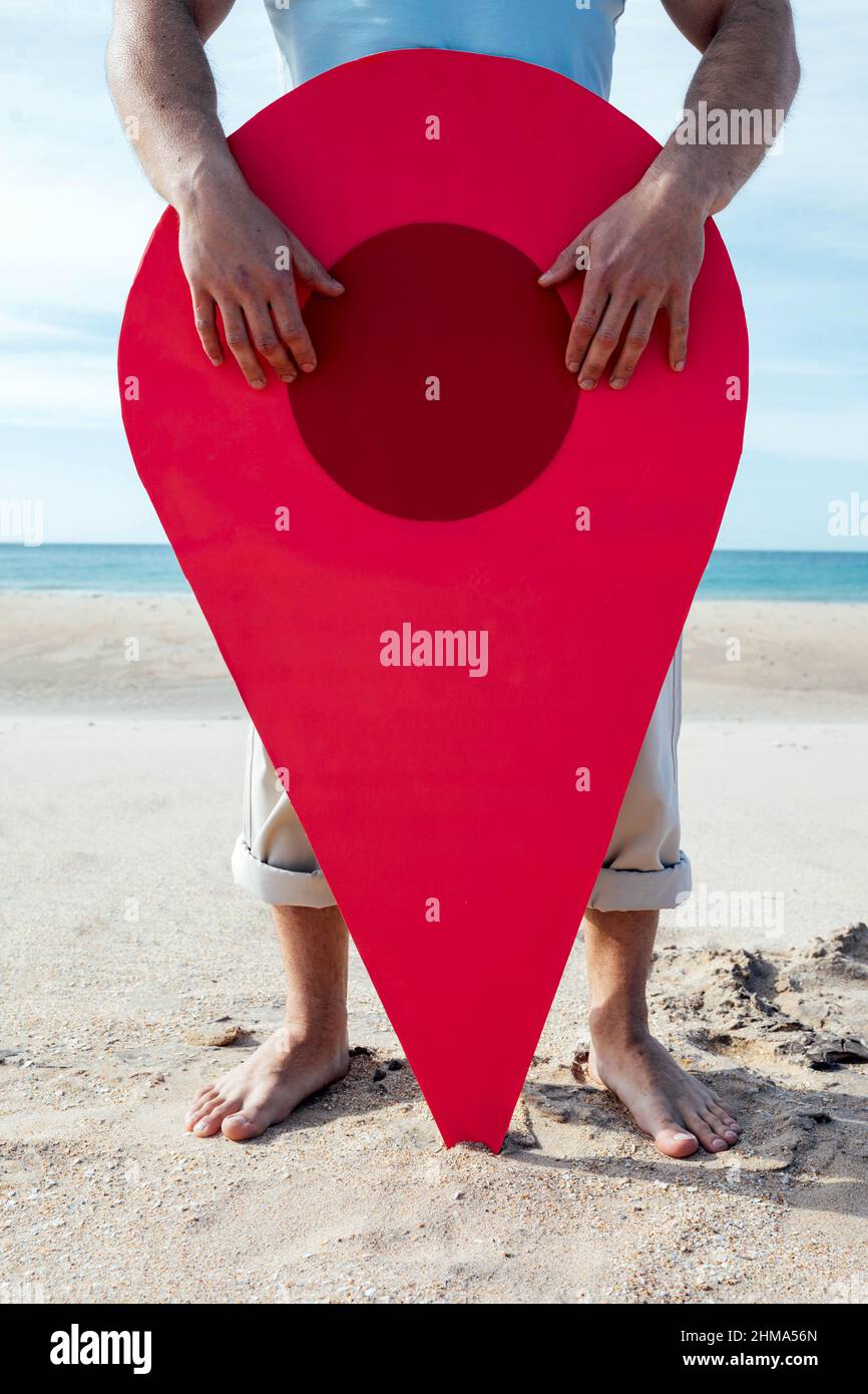 Raccolto turistico in piedi con pin rosso posizione sulla spiaggia sabbiosa contro il mare e alla ricerca di direzione Foto Stock