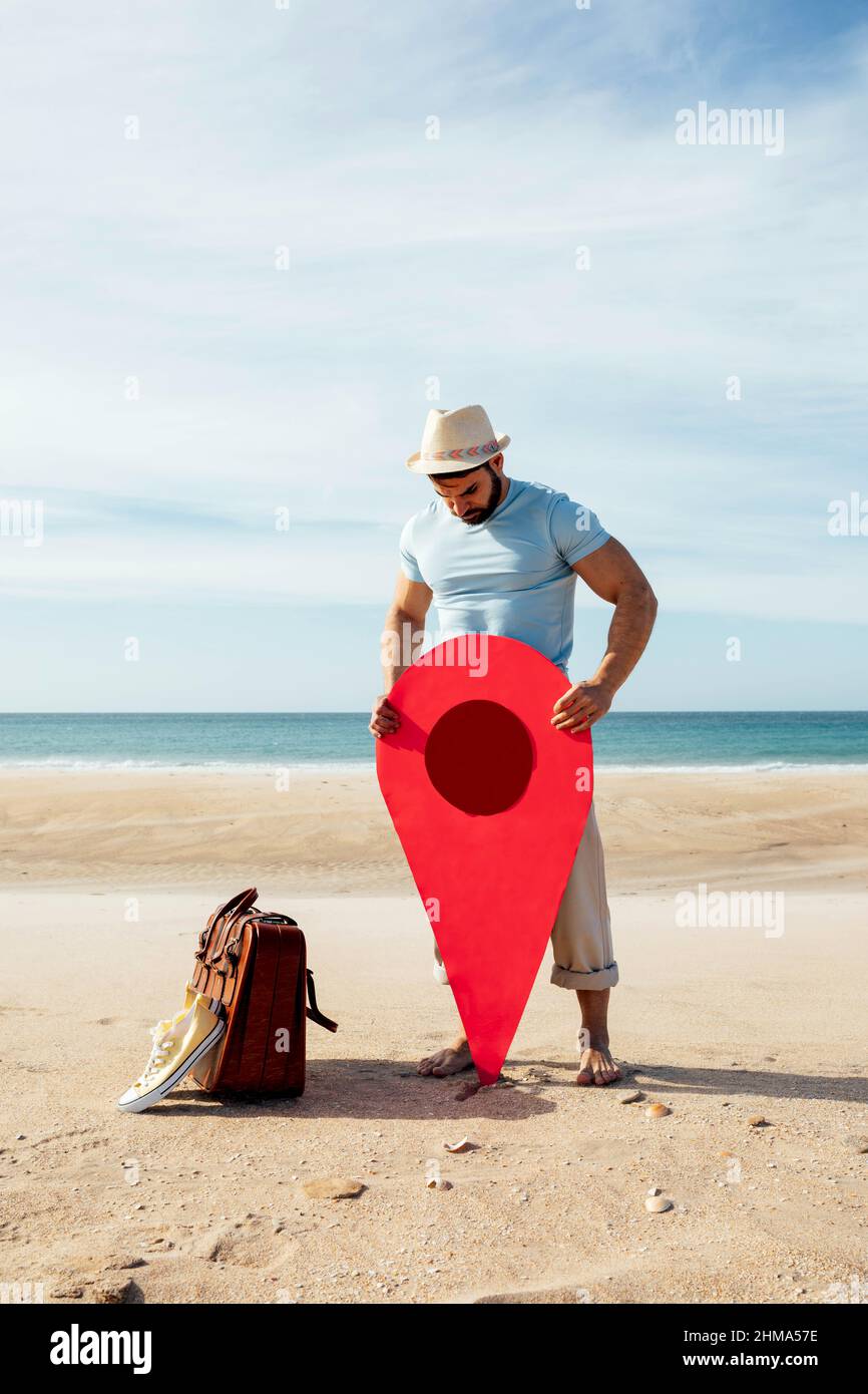 Perso maschio turista in piedi con pin posizione rossa sulla spiaggia di sabbia contro il mare e alla ricerca di direzione Foto Stock