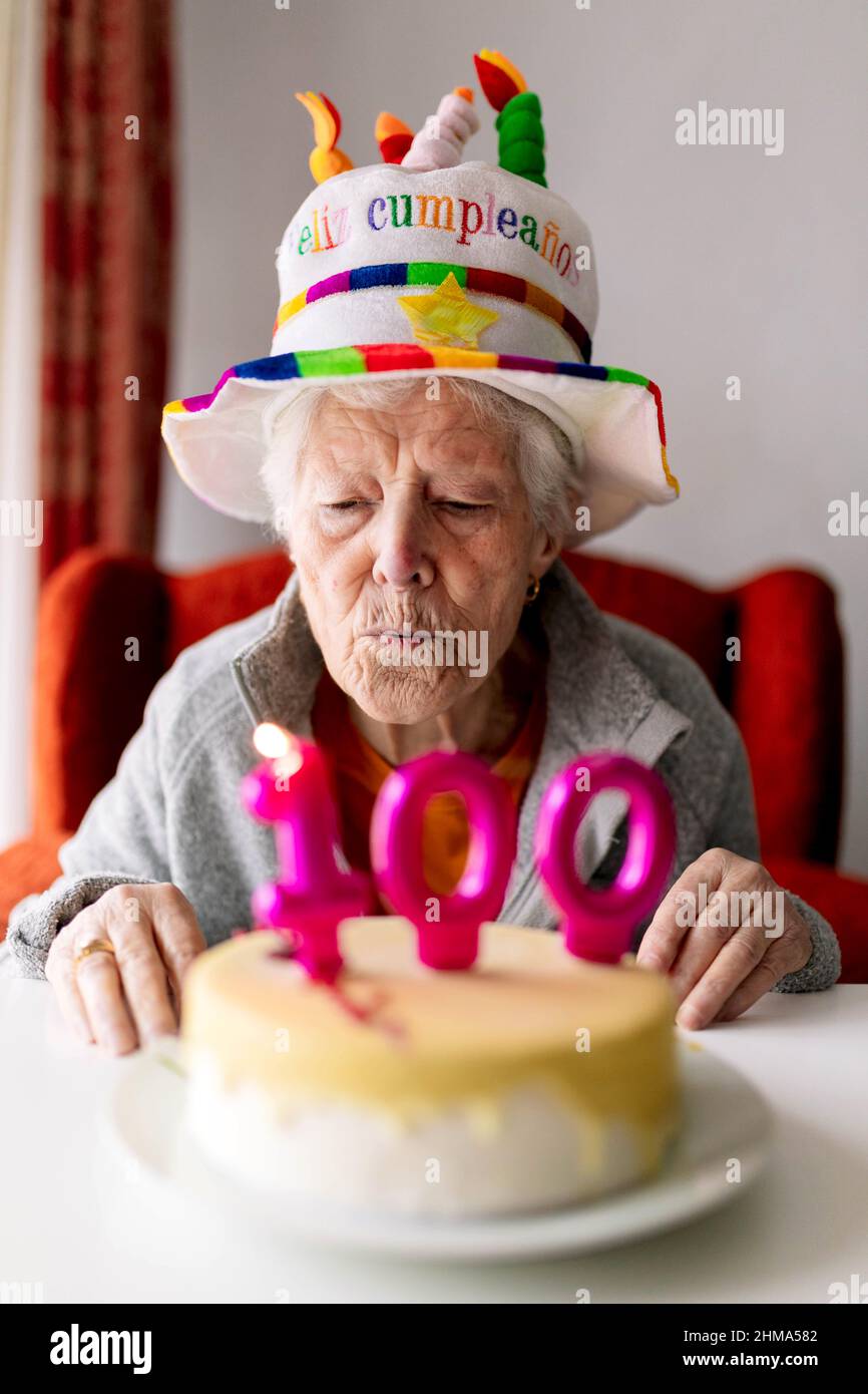 Donna anziana in cappello divertente soffiando candele brucianti con il  numero 100 sulla torta di compleanno e celebrare l'anniversario a casa Foto  stock - Alamy