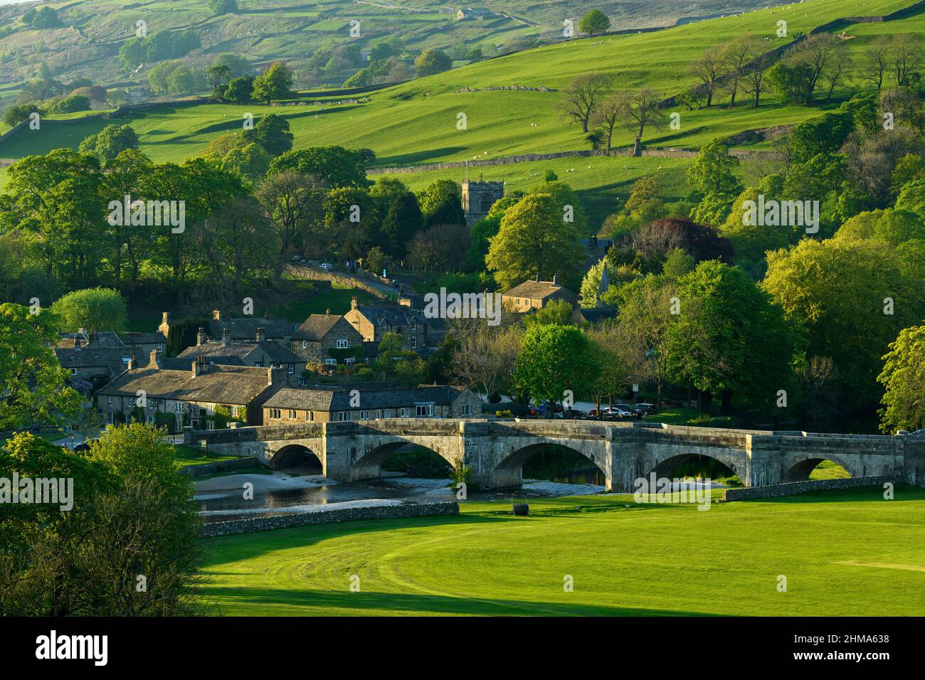 Panoramica Burnsall soleggiato immerso nella valle (5-arched ponte, case attraenti, chiesa torre, verde collina campi) - Yorkshire Dales, Inghilterra, Regno Unito. Foto Stock