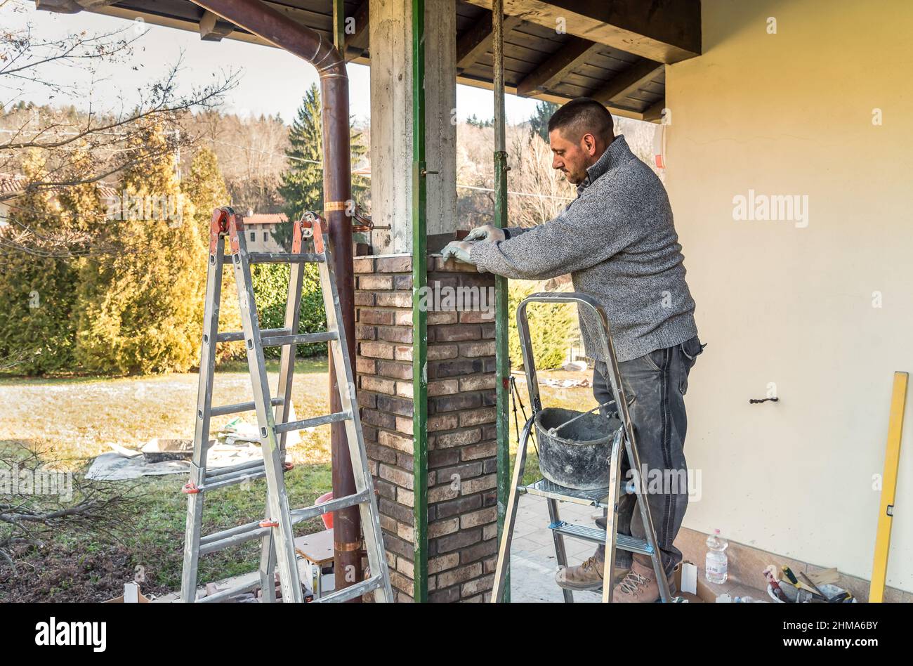 Muratore che installa mattoni sul pilastro esterno di calcestruzzo della casa. Lavoro di costruzione che posa mattoni. Foto Stock