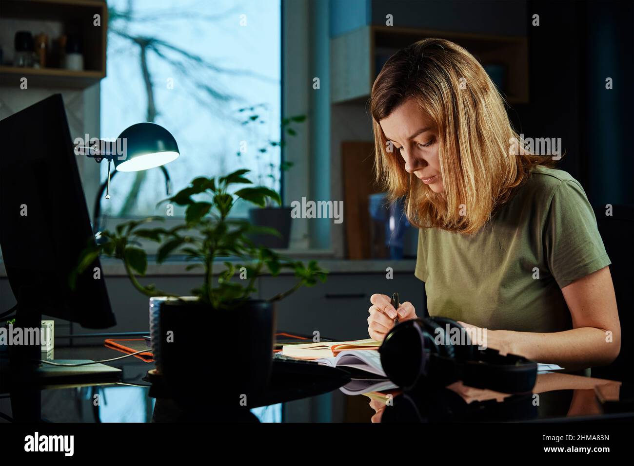 Donna seduta al tavolo in ufficio a casa e lavora con il computer. Freelance che lavora in remoto in ritardo. Stress emotivo e burnout Foto Stock