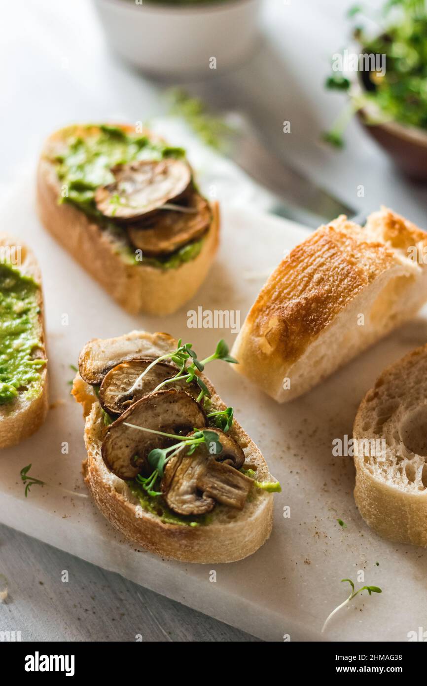 Baguette con guacamole, funghi champignons e micro verde su piatto bianco. Brunch idee. Fonte di proteine vegane. Cibo sano. Mangiare pulito. Foto Stock