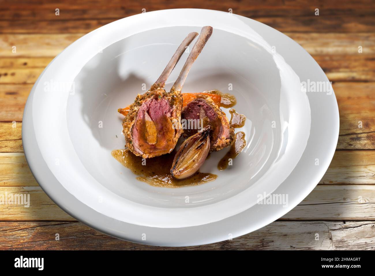 Costolette di agnello farcite di fegato al forno con scalini in piatto bianco su tavola di legno Foto Stock