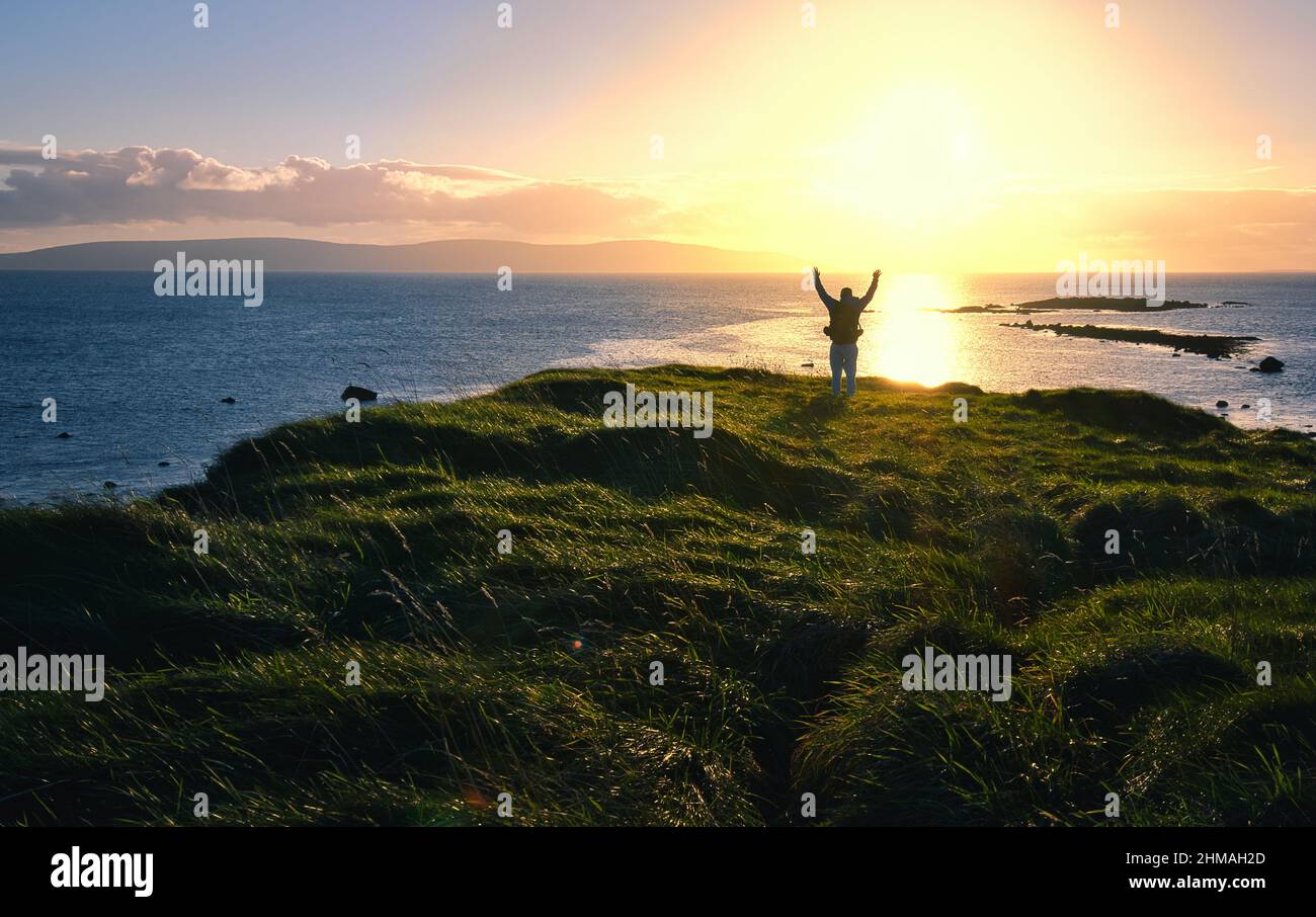 Tramonto paesaggio costiero con uomo silhouette sul bordo della scogliera a Cloosh, Galway, Irlanda Foto Stock