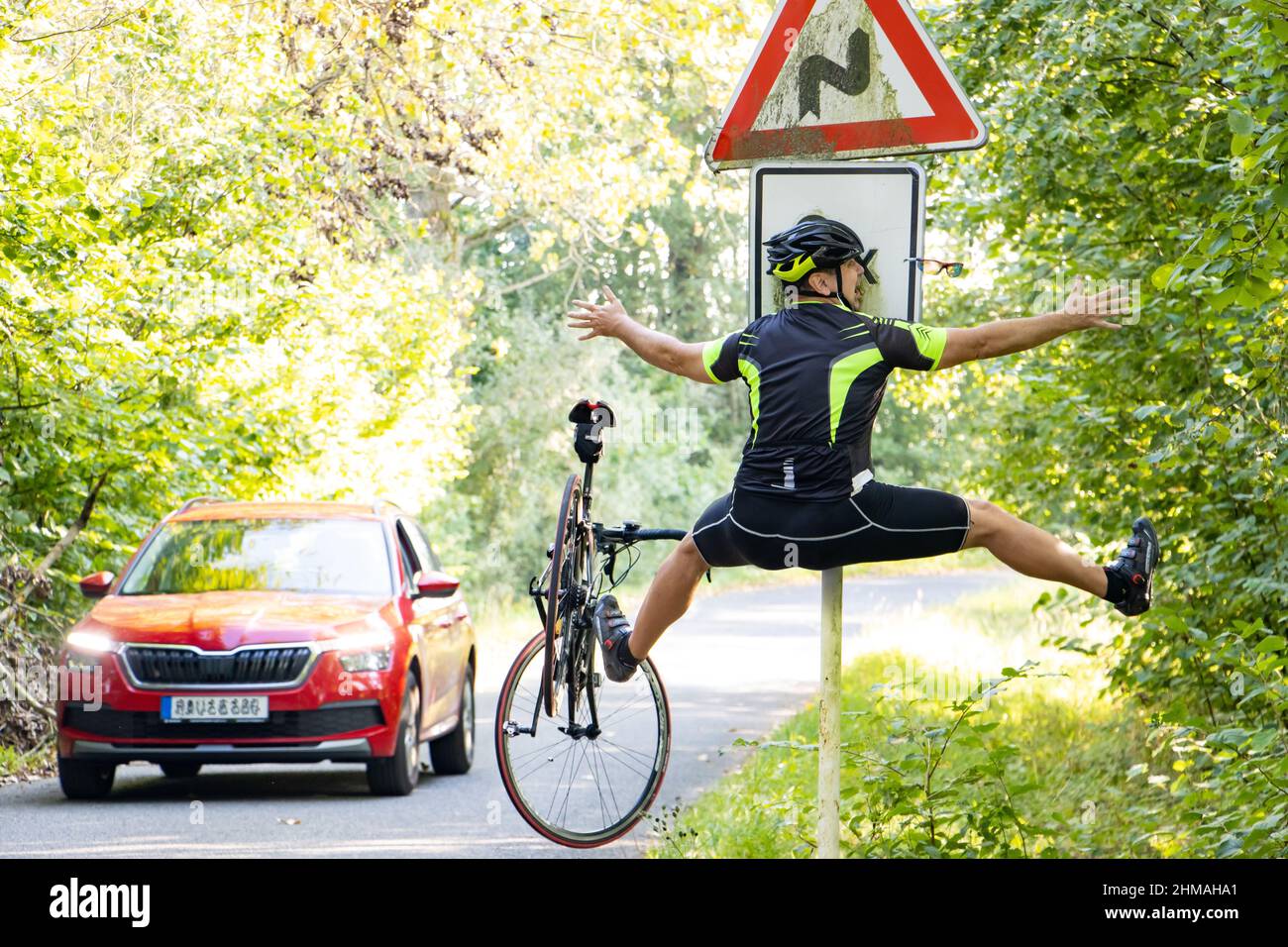Un ciclista che cade urta in un cartello stradale accanto alla strada con traffico Foto Stock