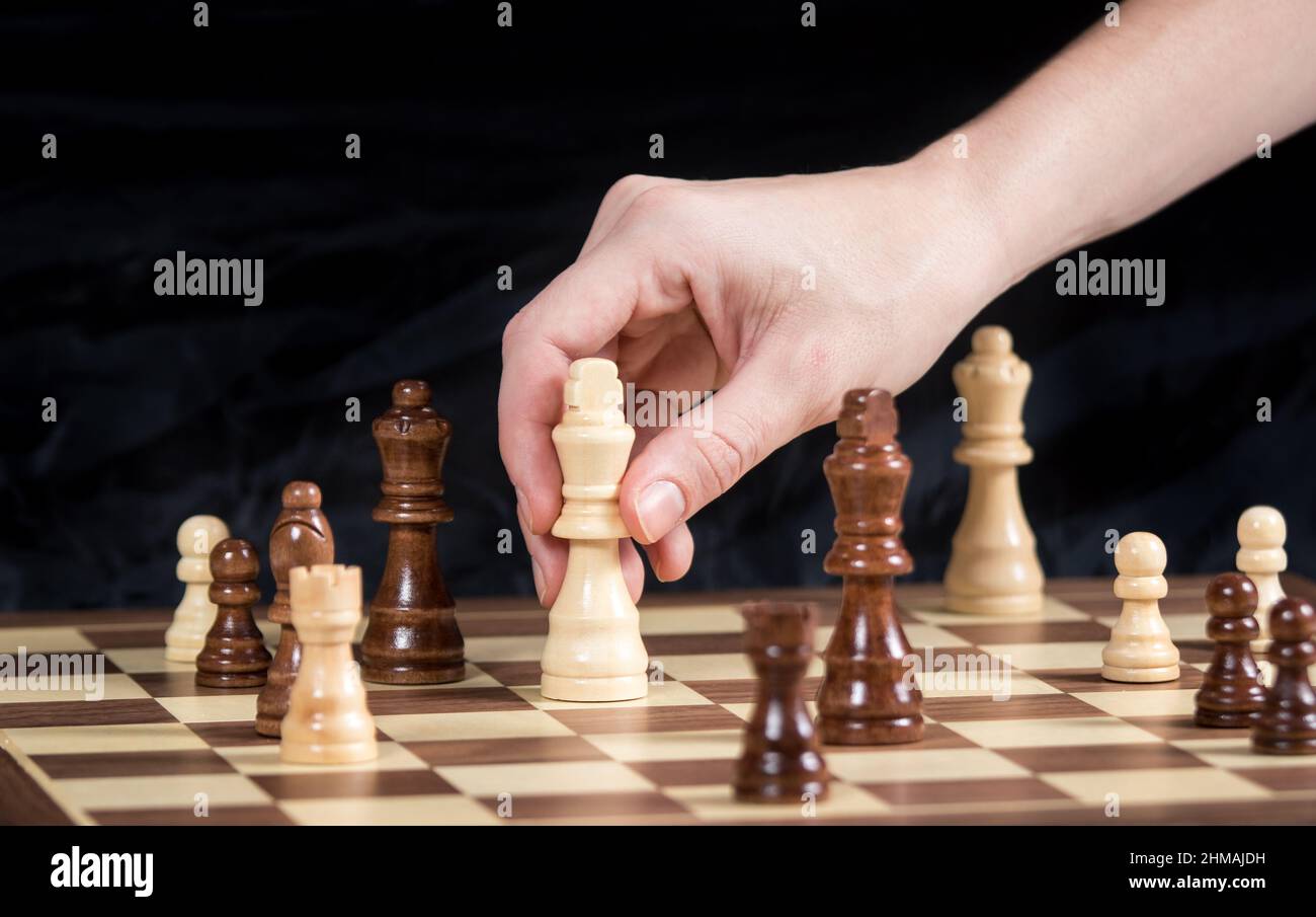 Persona che sposta pezzo di Scacchi Re durante una partita con sfondo scuro Foto Stock