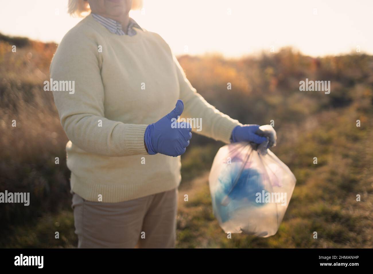 Giorno della terra. Purezza della natura. Donna pulup volontario attivista in guanti di gomma mano mette un sacchetto di plastica spazzatura in un sacco di rifiuti, raccogliendo rifiuti Foto Stock