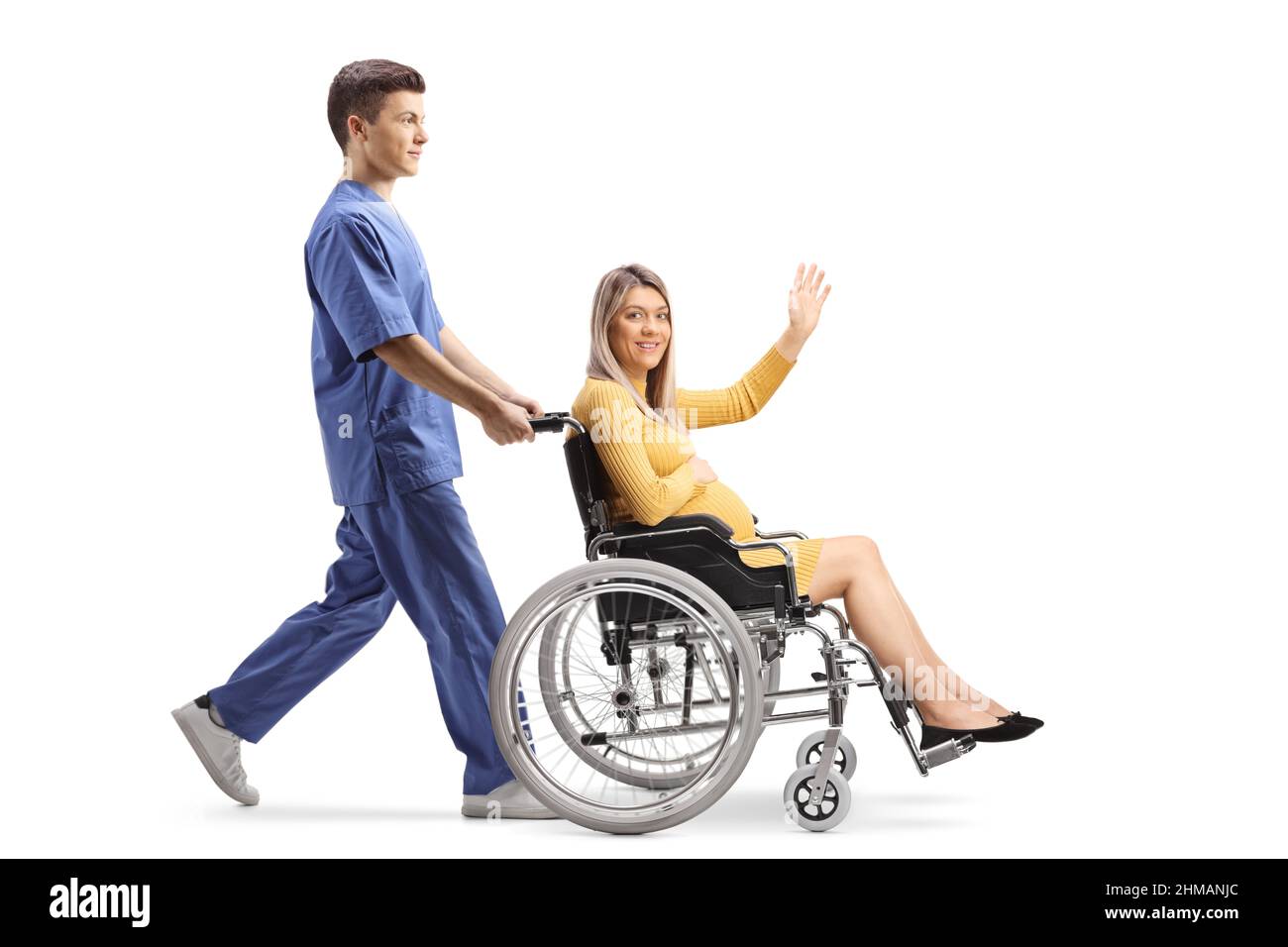Scatto a profilo completo di un'infermiera maschio che spinge una donna incinta che ondita e siede su una sedia a rotelle isolata su sfondo bianco Foto Stock