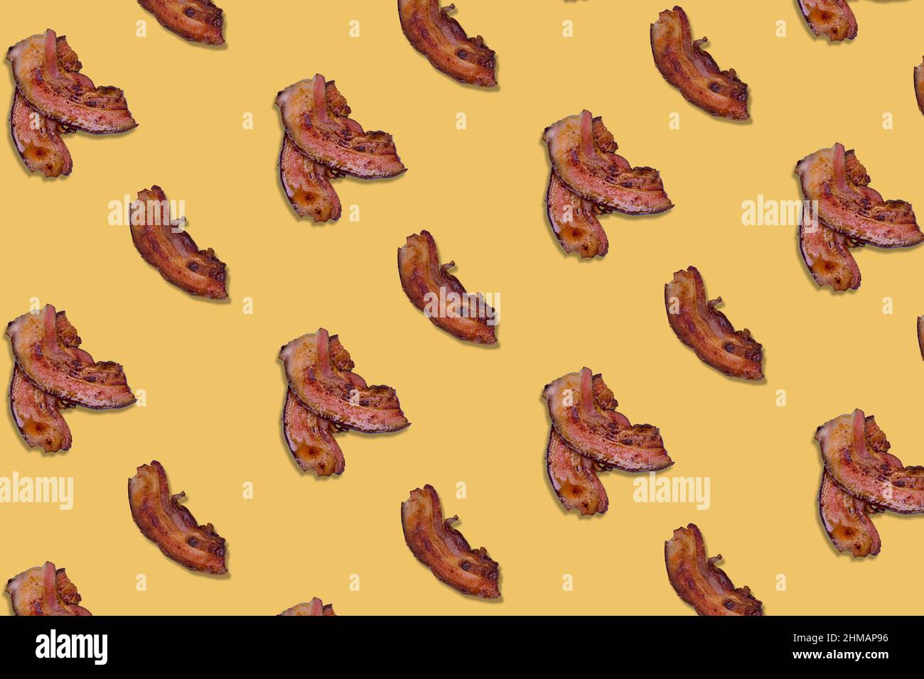 Il motivo ha fatto molte fette croccanti di pancetta su sfondo giallo. Colazione minimale e creativa. Vista dall'alto. Disposizione piatta. Foto Stock