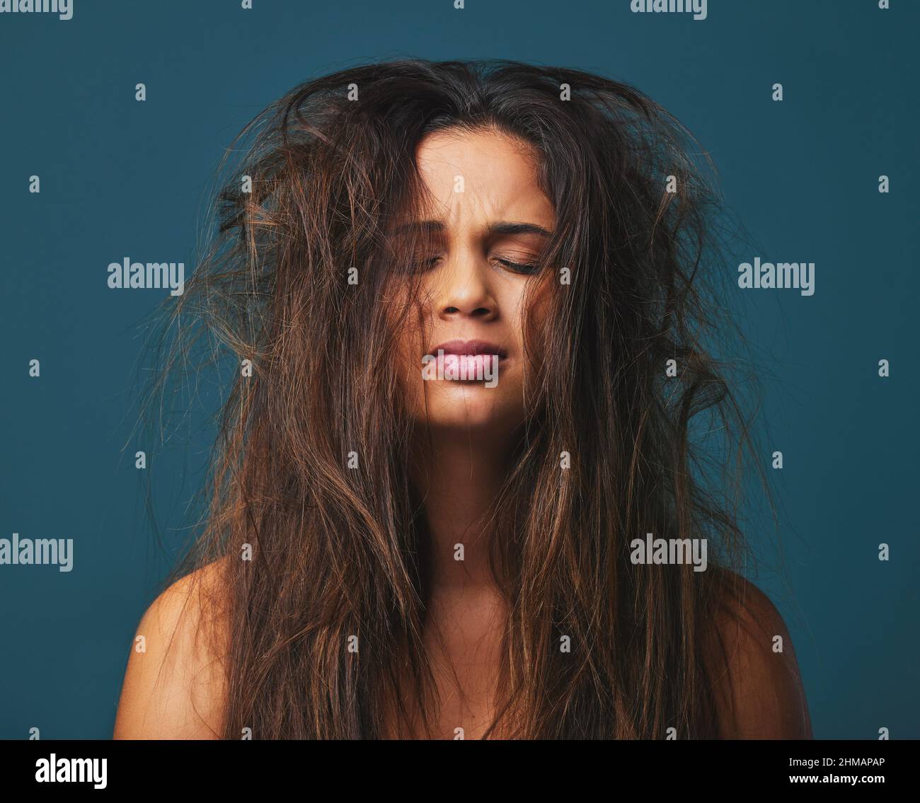 Il dolore che tenete li rende degno il vostro peso in oro. Studio girato di una bella giovane donna con capelli disordinati posando su uno sfondo blu. Foto Stock