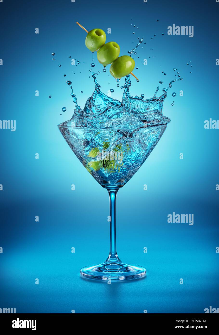 Bicchiere Martini con un incredibile spruzzi a causa della caduta di bacche d'oliva in esso. Sfondo blu. Foto Stock