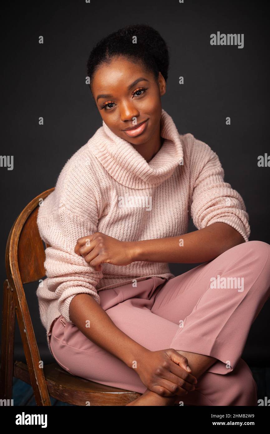Una donna nera che indossa un pullover dolcevita e pantaloni pesca Foto Stock