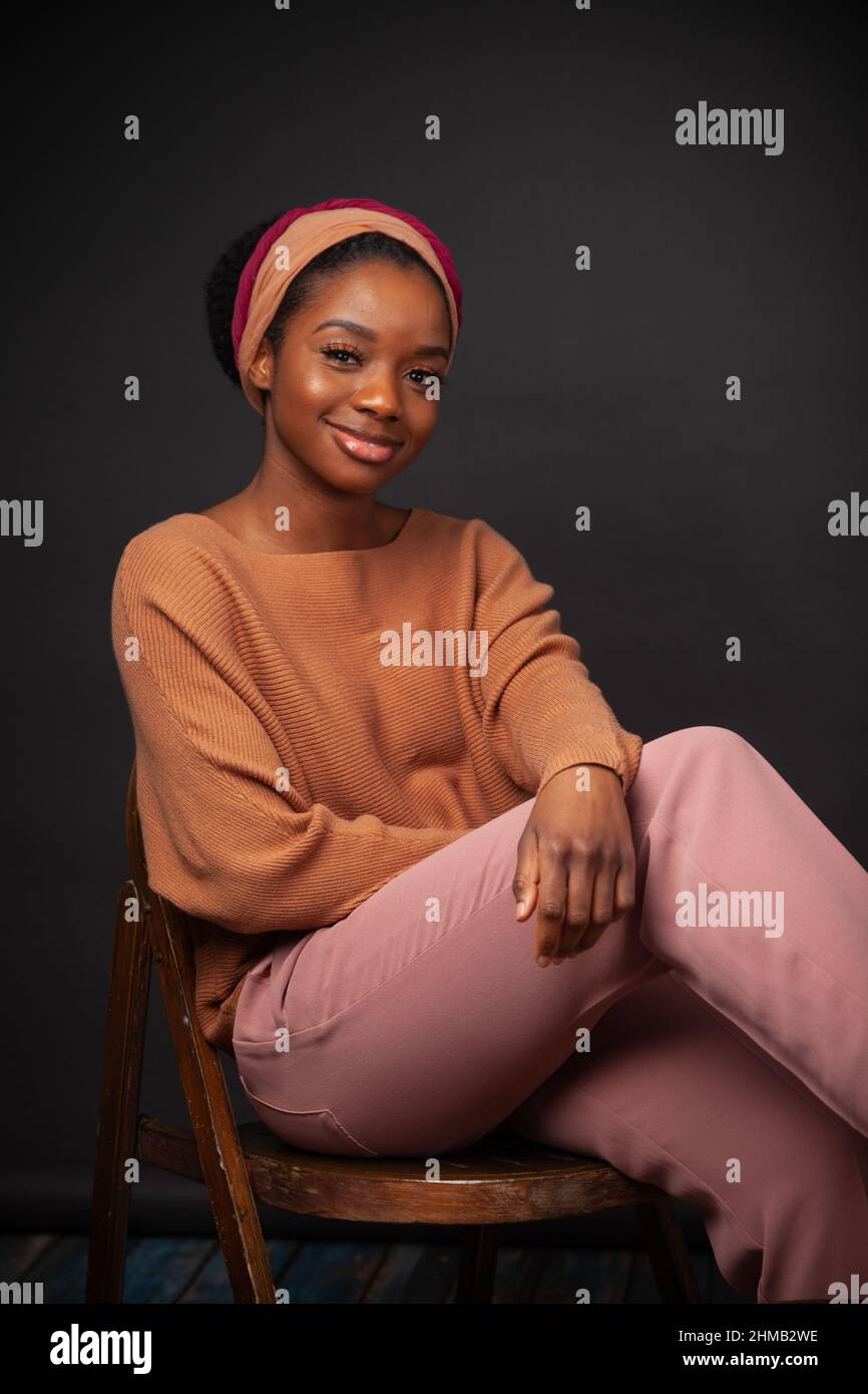 Una bella donna nera seduta giù indossando pantaloni pesca e un foulard Foto Stock